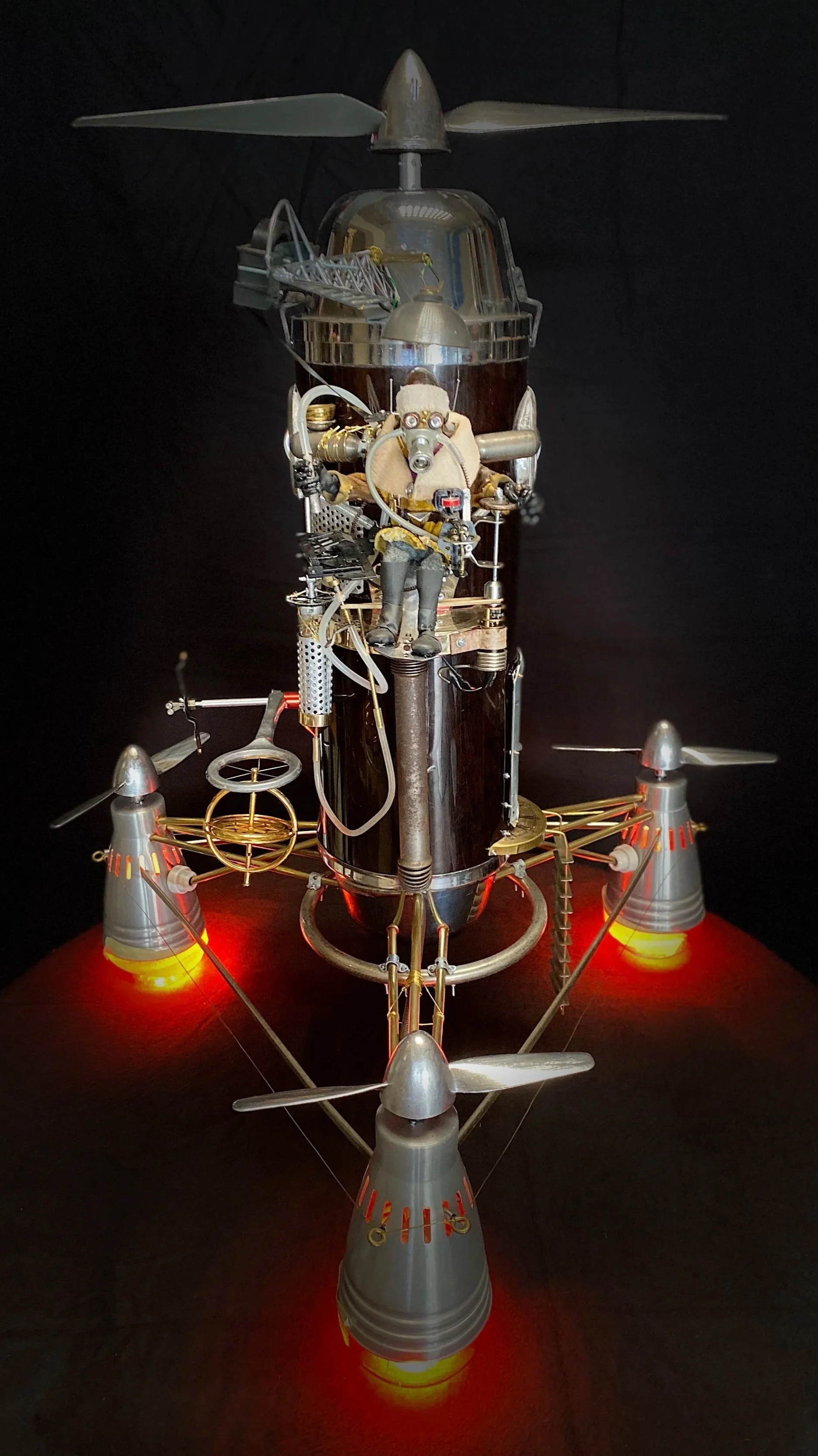 A detailed model of a lunar lander with a mounted astronaut figure, featuring multiple propellers, metallic surfaces, and reddish lights illuminating its landing legs.