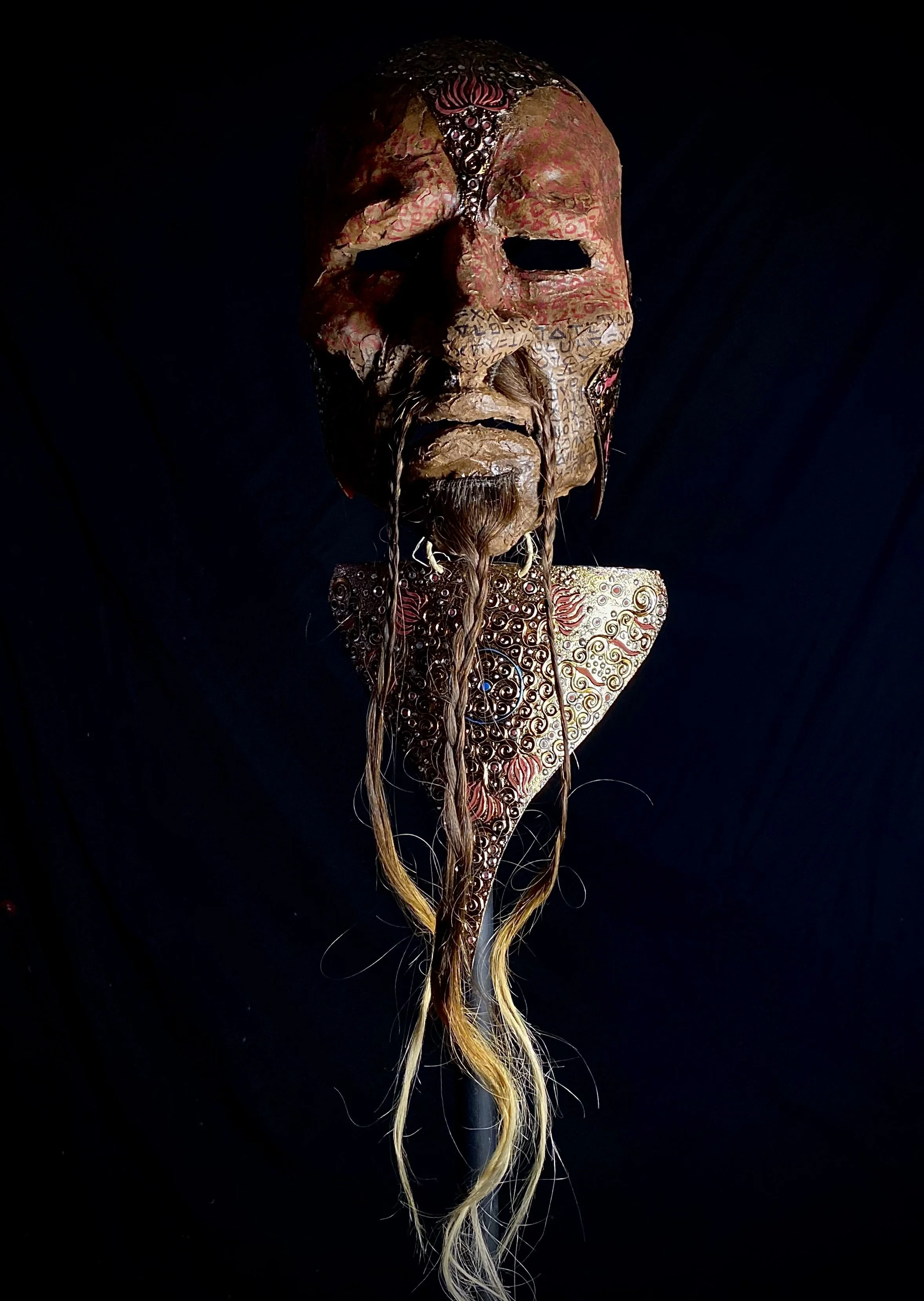 An elaborate tribal mask with detailed patterns, long hair, and a dark background.