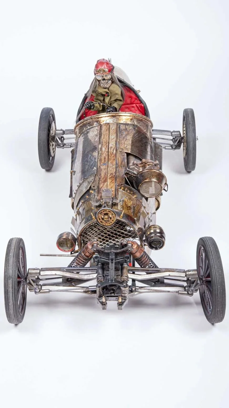 A vintage race car with a skeleton driver figure wearing goggles and a red cap, set against a plain white background.