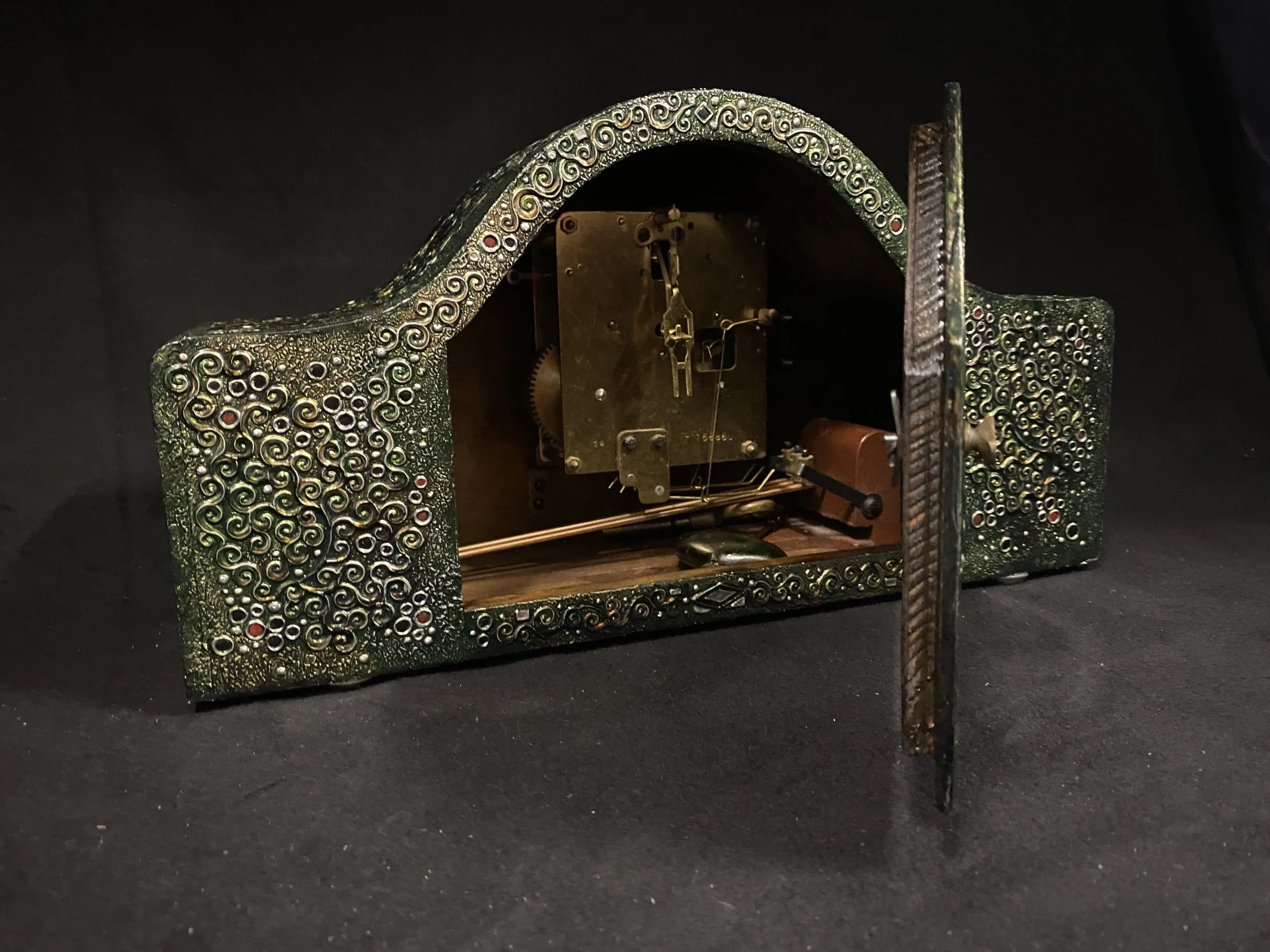 An antique clock case with intricate green and gold scrollwork, showing internal gears and mechanisms.