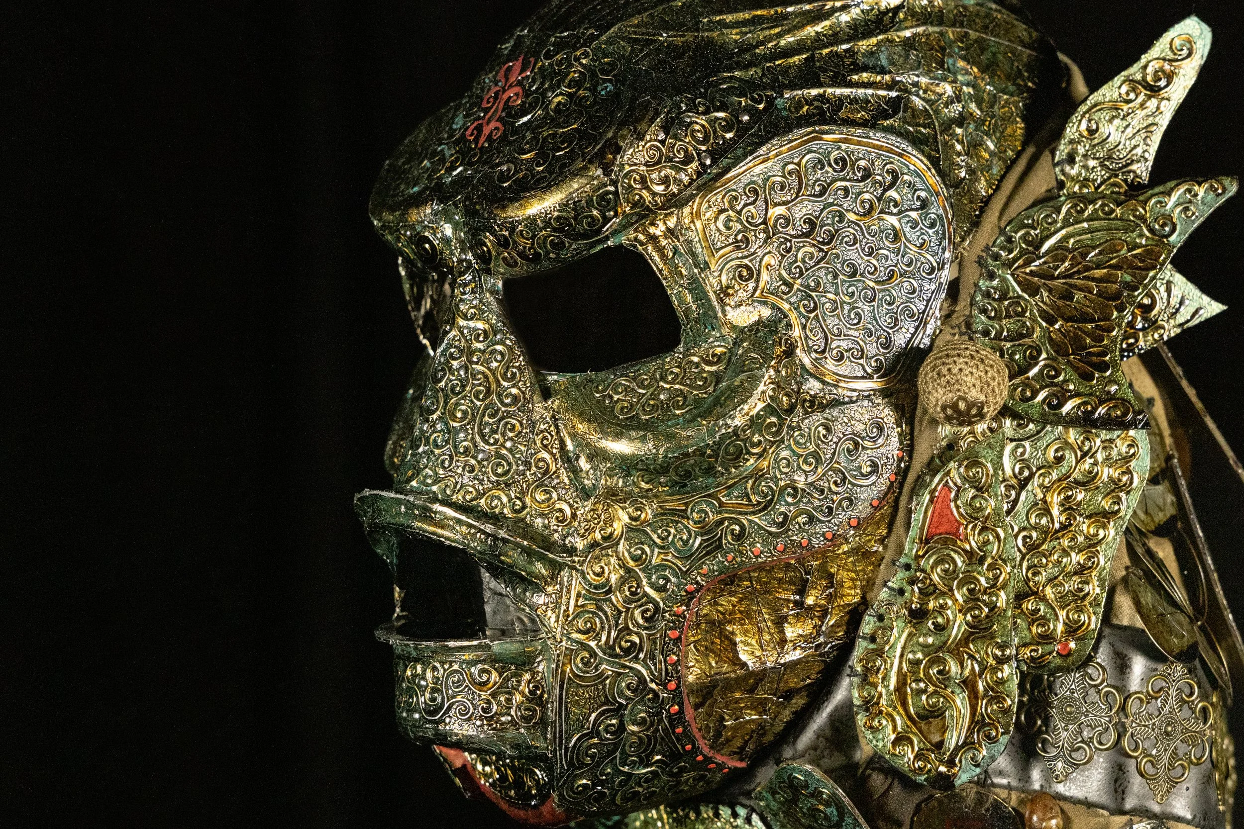Close-up of an ornate, decorative mask with intricate gold and black patterns and embellishments, resembling a traditional or ceremonial design.
