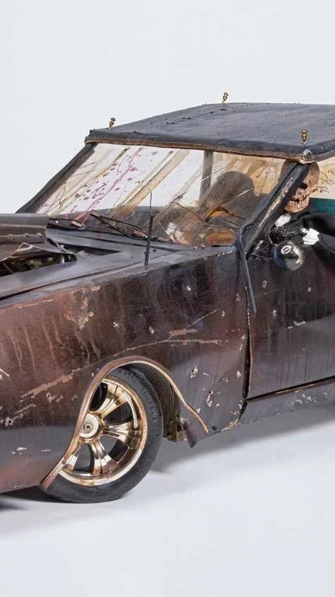 A worn-out, rusty black vintage convertible car with a torn soft top, missing paint, and a damaged body, placed indoors.