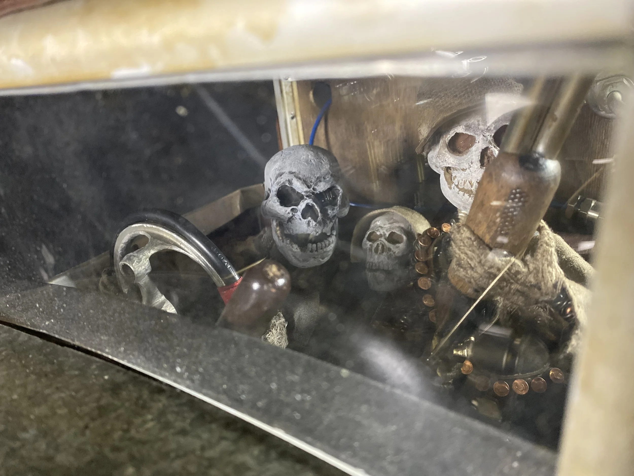 Several small skull figurines inside a glass display, surrounded by mechanical parts and tools.