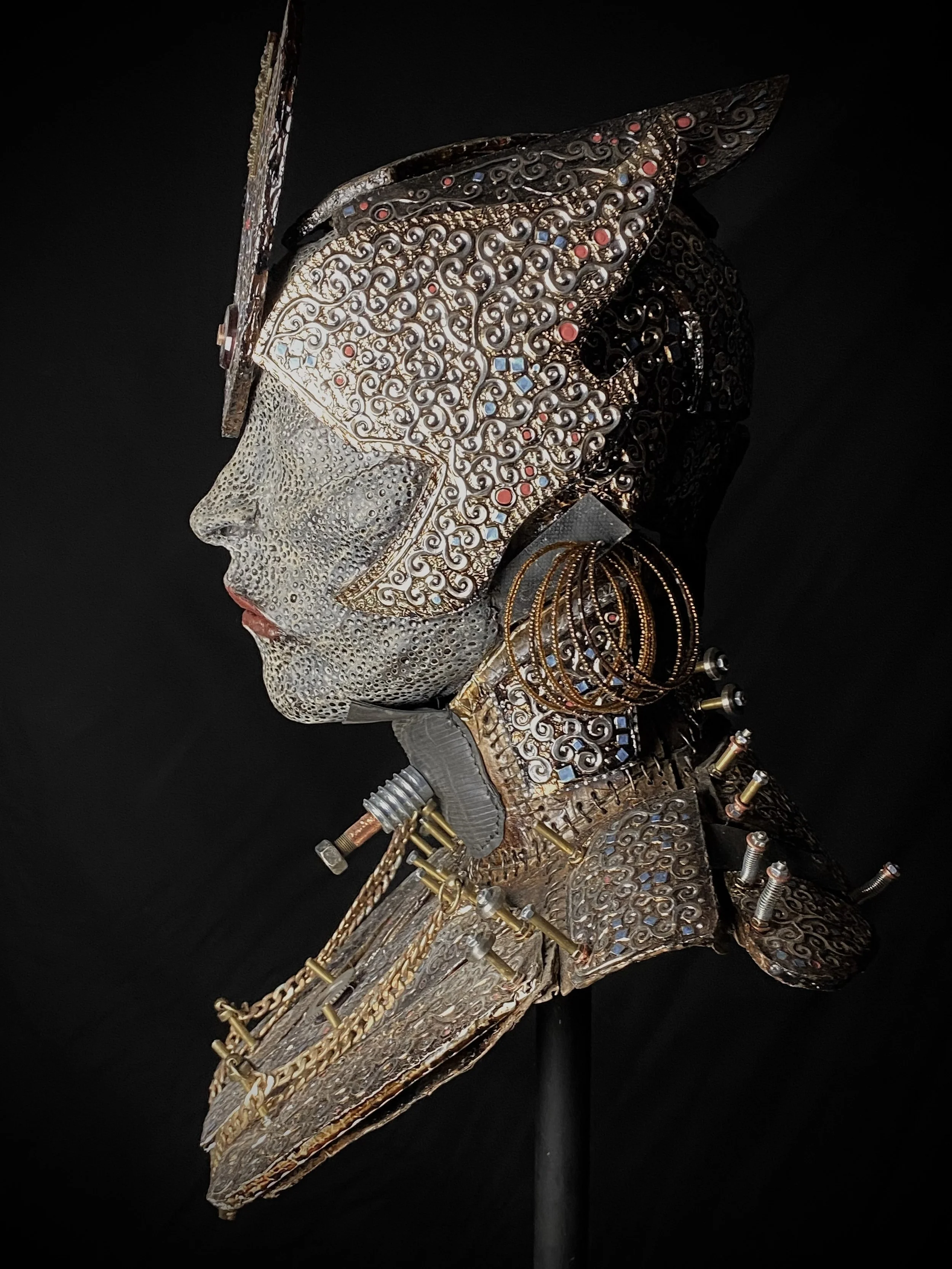 A mixed media sculpture of a woman's profile, combining metal, jewelry, and electronic components, set against a black background.