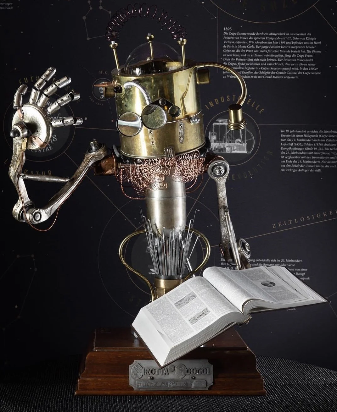 A steampunk-inspired robot sculpture made of metallic parts, holding a wrench in one hand, with an open book on a wooden stand in front of it. The background features information in German and diagrams.