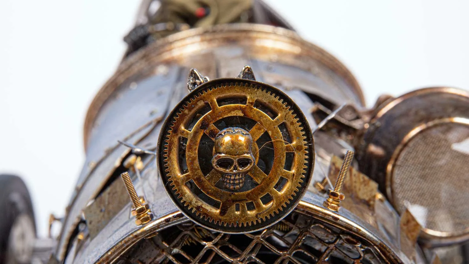 Close-up of a vintage mechanical device with a brass skull and gear design, surrounded by wires and metal parts.
