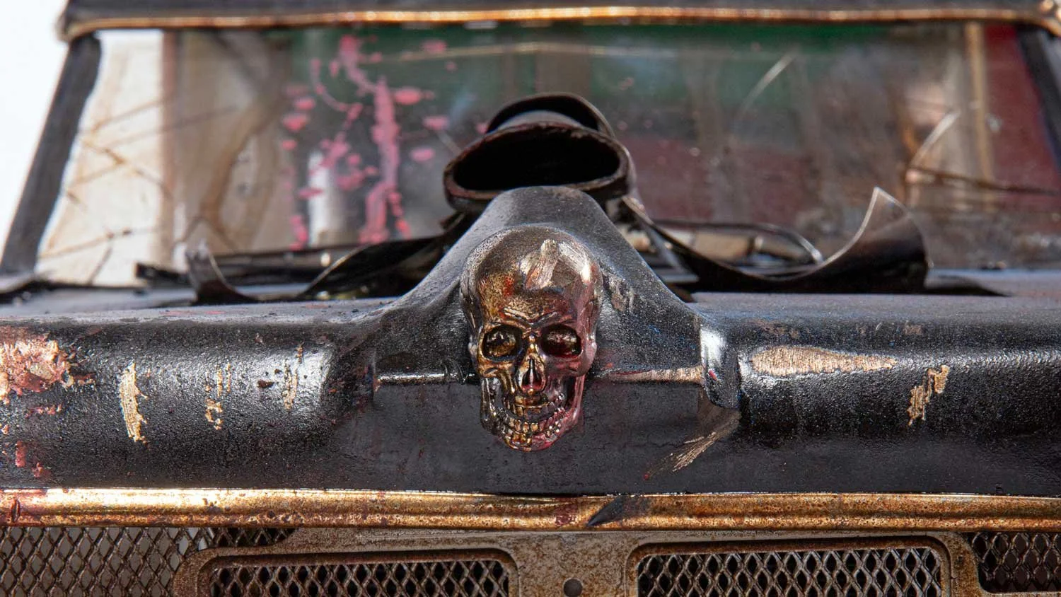Close-up of an old, rusty vehicle with a skull emblem on the front grille.