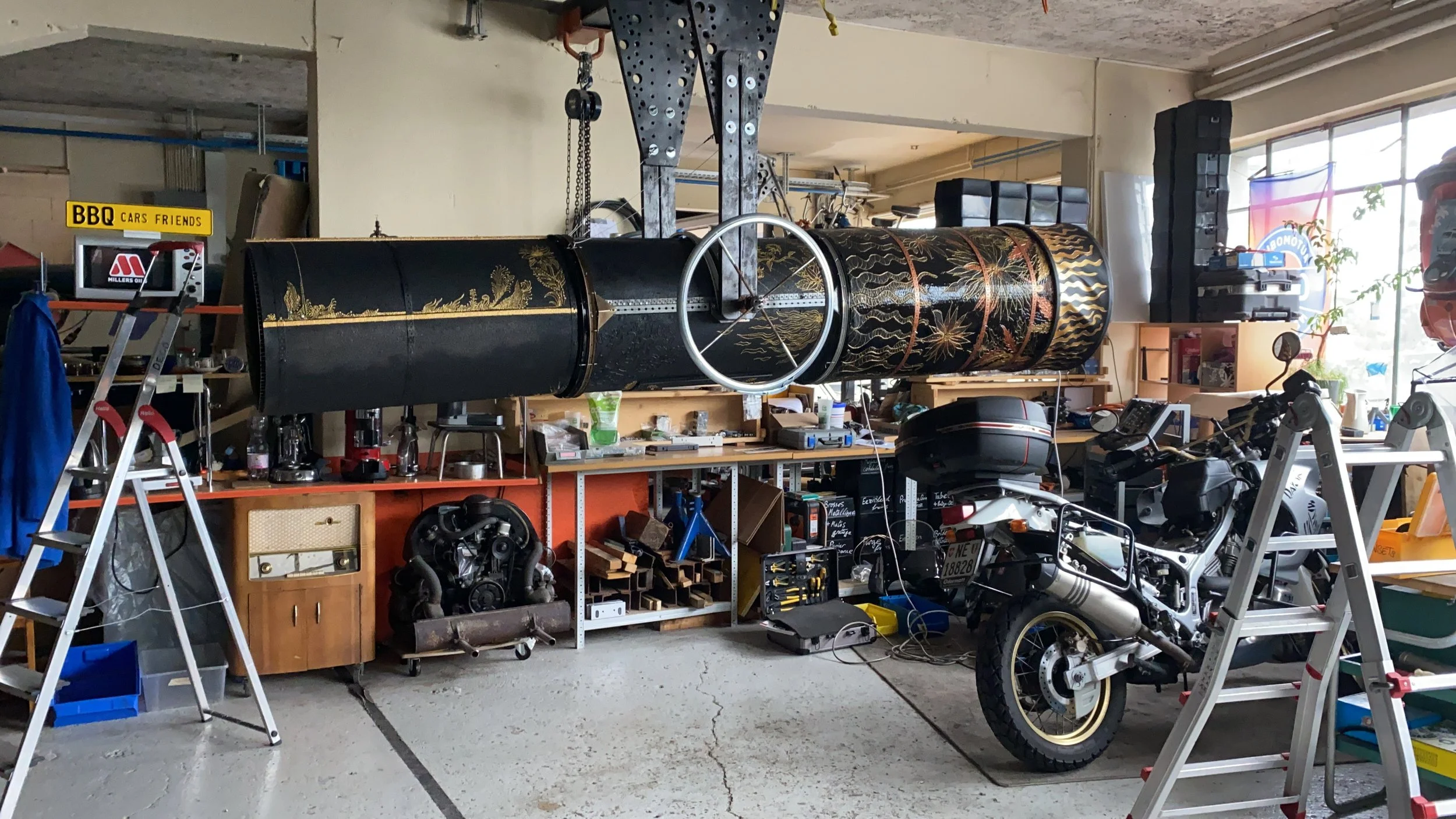 Garage filled with tools, motorcycle, and a large black and gold decorative cylindrical structure hanging from the ceiling.