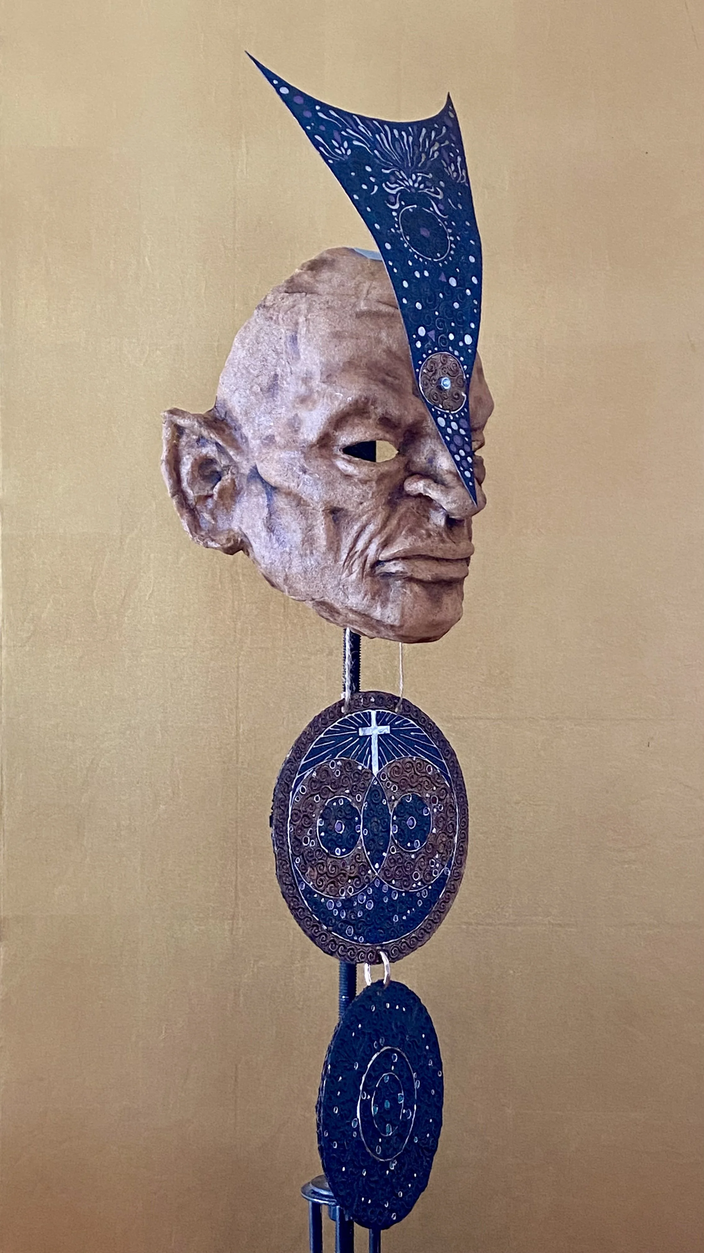 Mixed media sculpture featuring a carved wooden human head with three painted circular discs and a blue painted metal piece attached to the head.