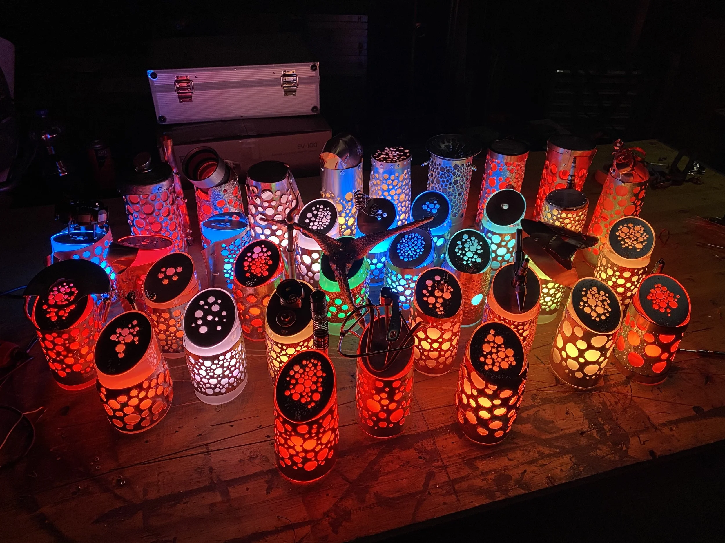 Multiple colorful incense or candle holders with perforated designs emitting red, blue, yellow, green, and white light, arranged on a wooden surface in a dimly lit setting.
