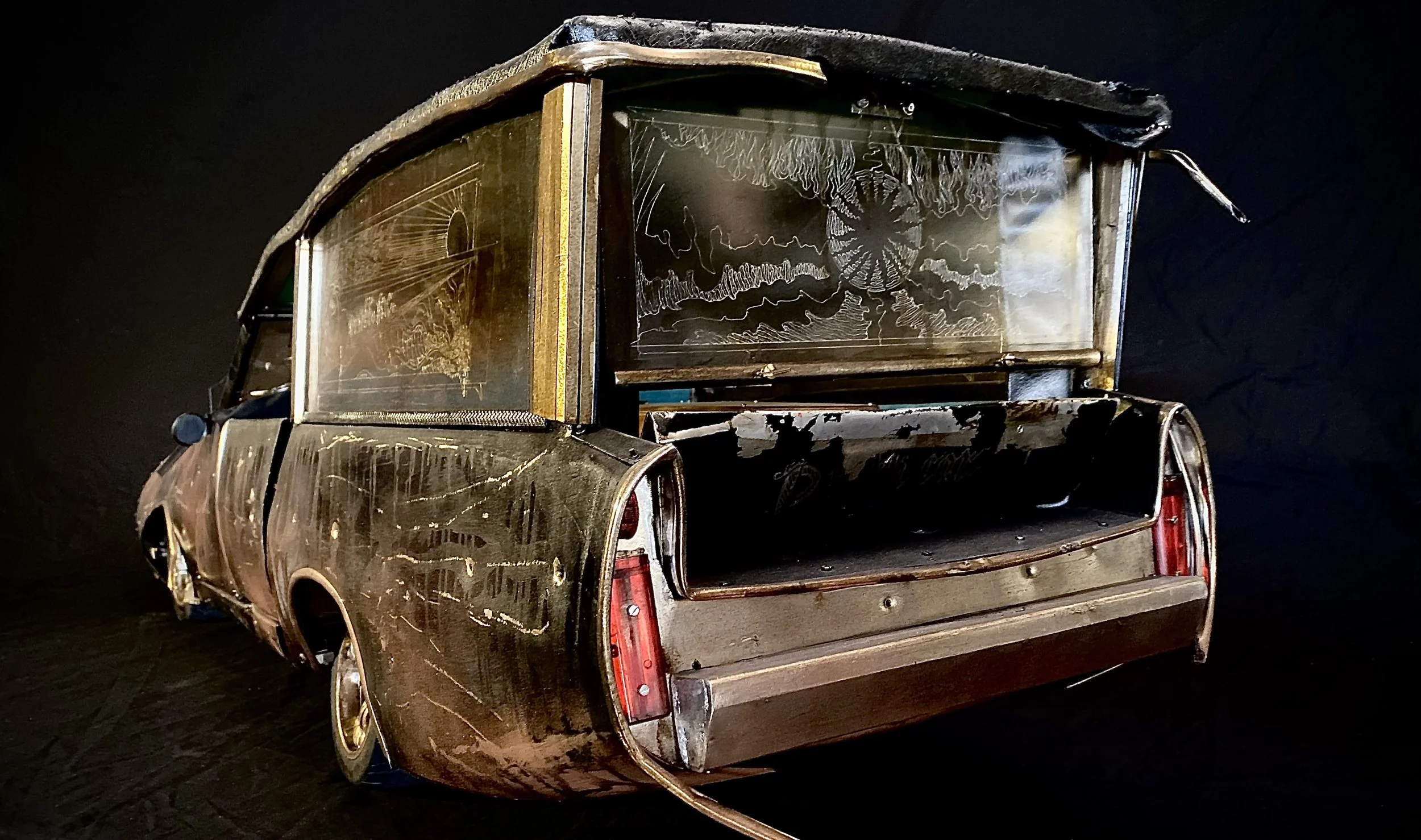 A vintage car with a metallic, reflective surface and an open trunk, featuring artistic etched glass windows with intricate designs, set against a dark background.