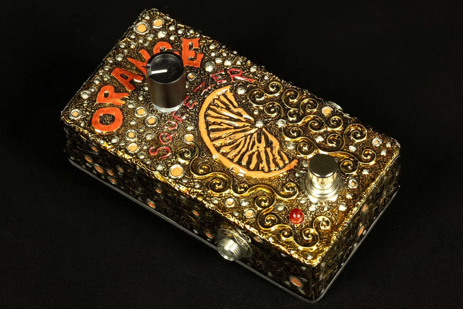 A decorative guitar effects pedal with a gold and black swirl pattern, red lettering, and a lemon slice illustration on top.