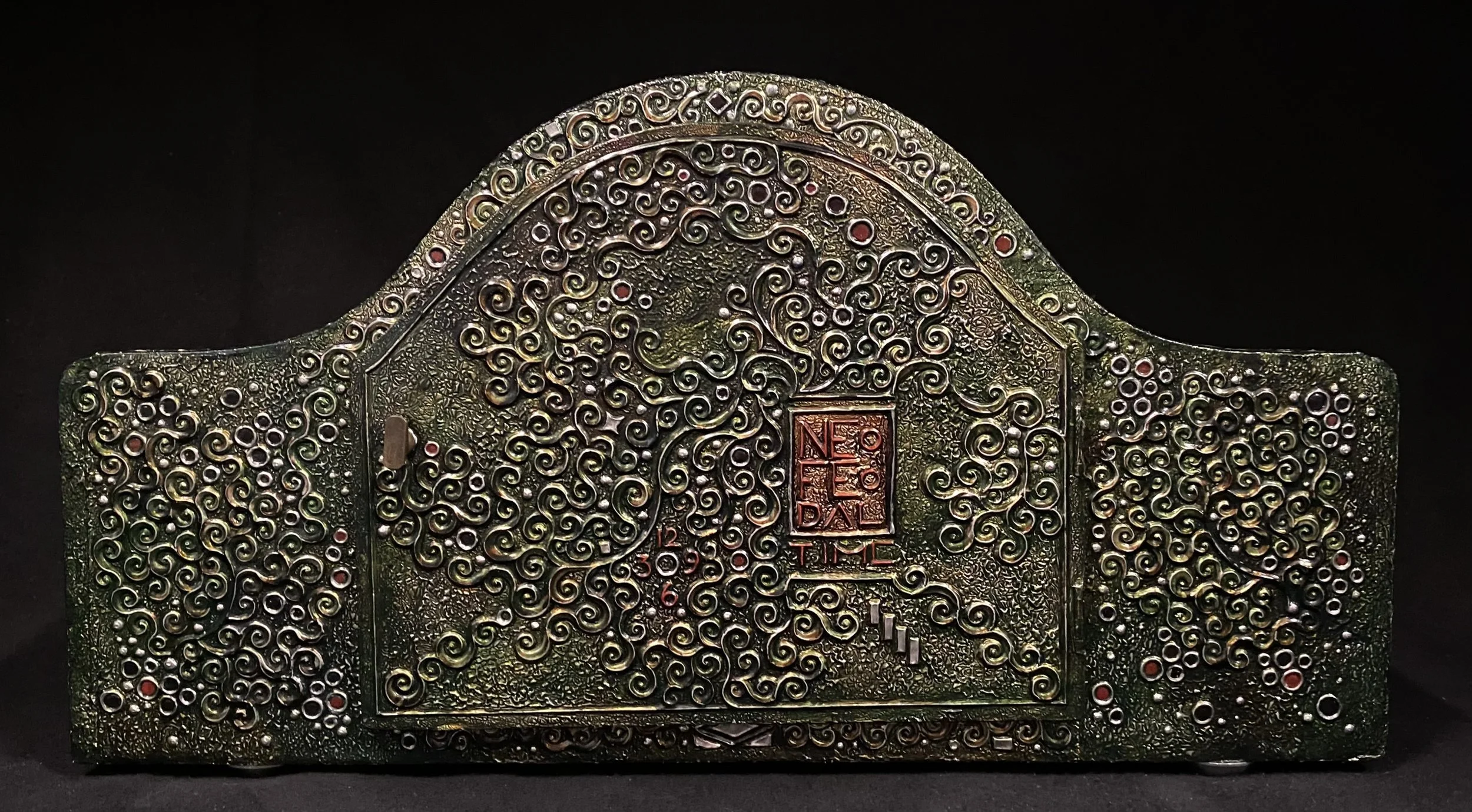 Decorative metallic plaque with intricate swirling patterns, a red rectangular stamp with Chinese characters, and small colorful accents, set against a black background.