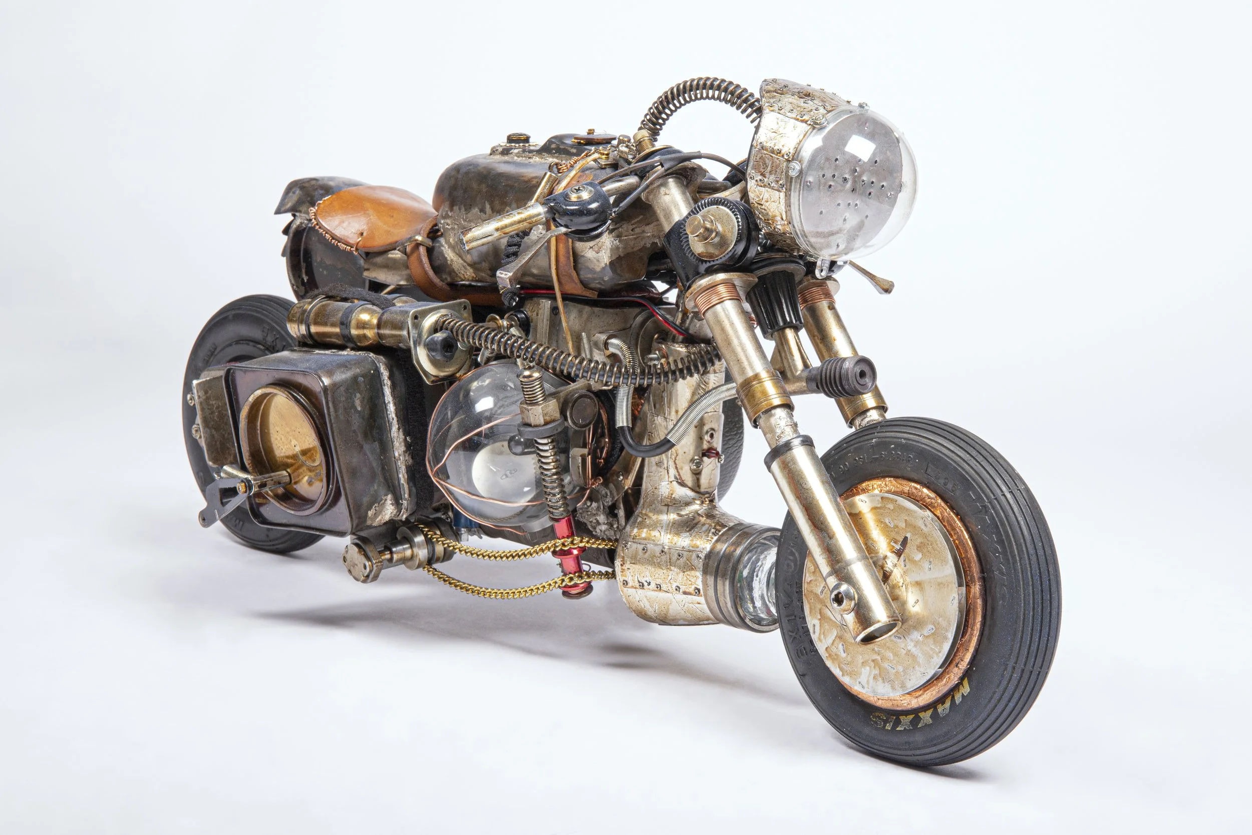 Steampunk style motorcycle made of metal and vintage parts with brass, copper, and steel components, featuring exposed wires, gears, and leather accents against a white background.