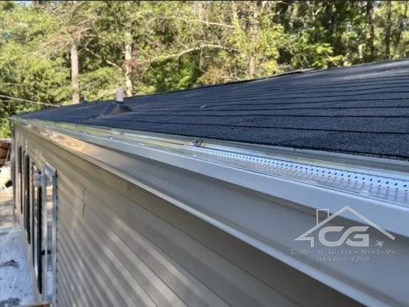Close-up view of a house's roof and 6 inch seamless gutter system with leaf guard in a wooded area.