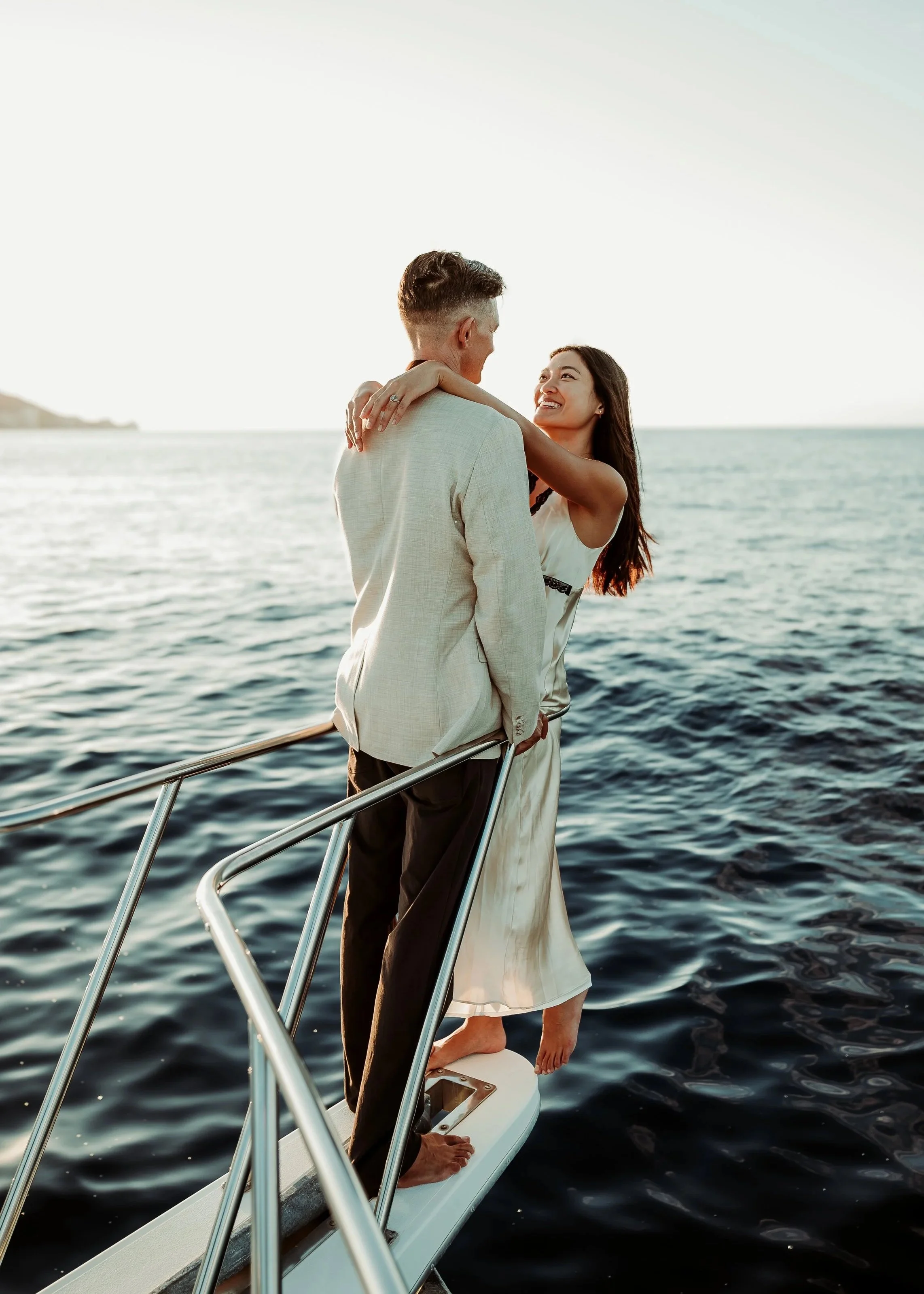 A couple standing on a yacht, embracing each other with smiles, by the water during sunset in Waikiki  | Best Hawaii Wedding Photographer & Videographer | Oahu, Hawaii Island, Kauai, and Maui