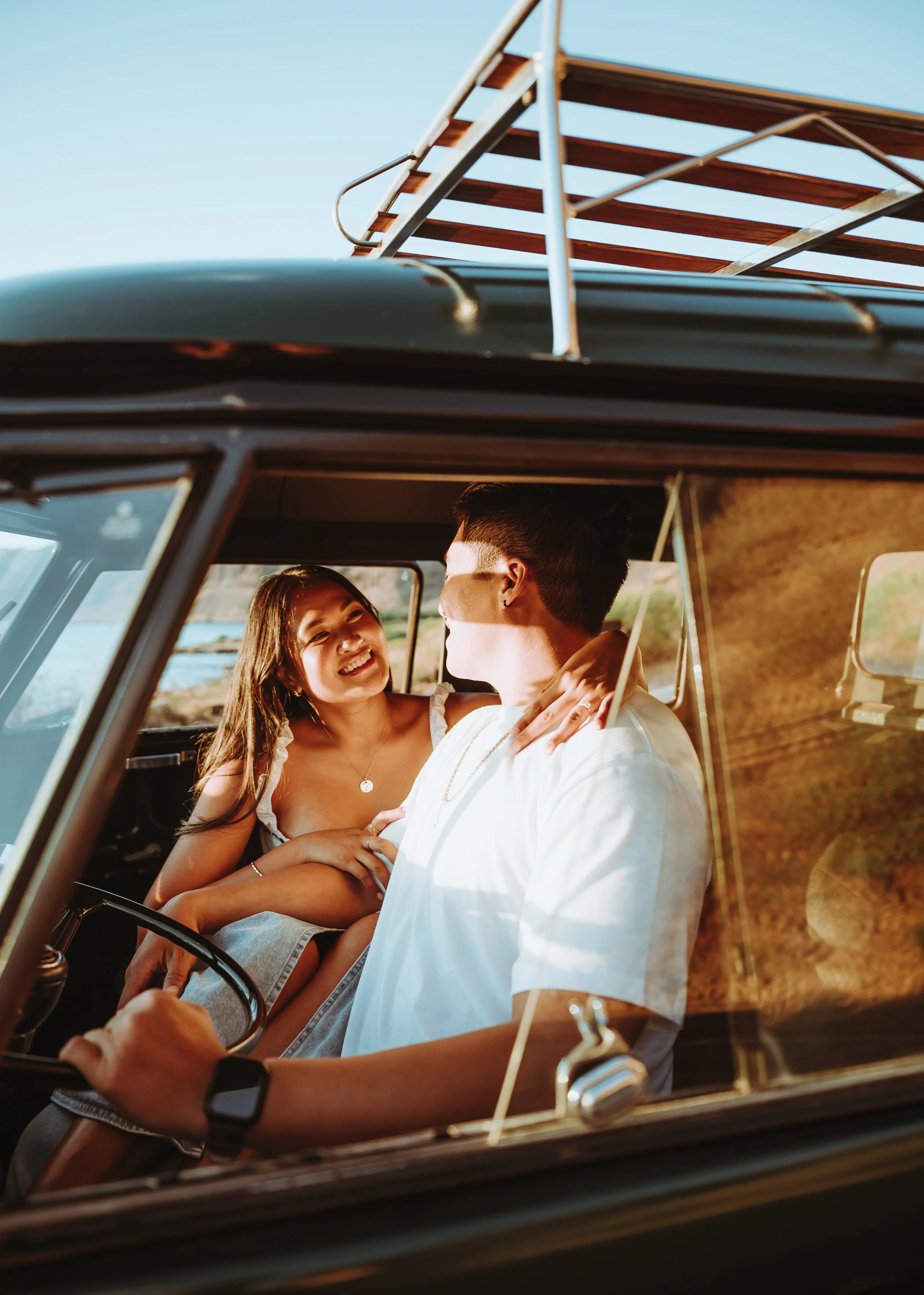 A young woman and a young man in a vintage vehicle, sharing a joyful moment, with the woman smiling and looking at the man, in a sunny outdoor setting.