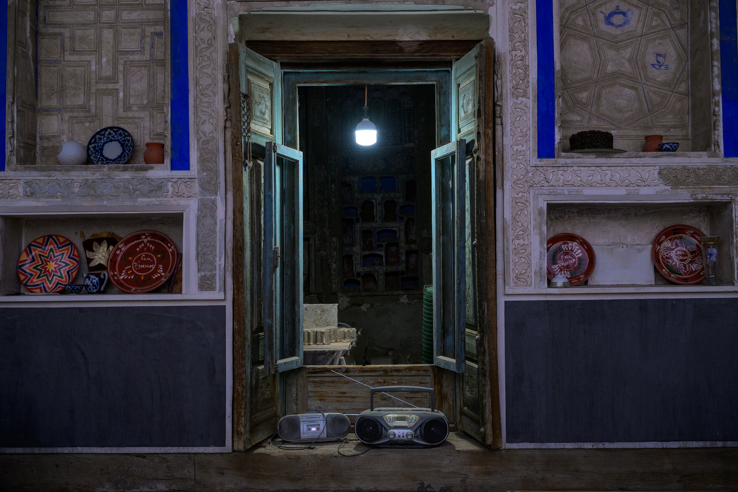 Room with decorated shelves, open wooden window, and a portable radio with a speaker, placed on the floor.