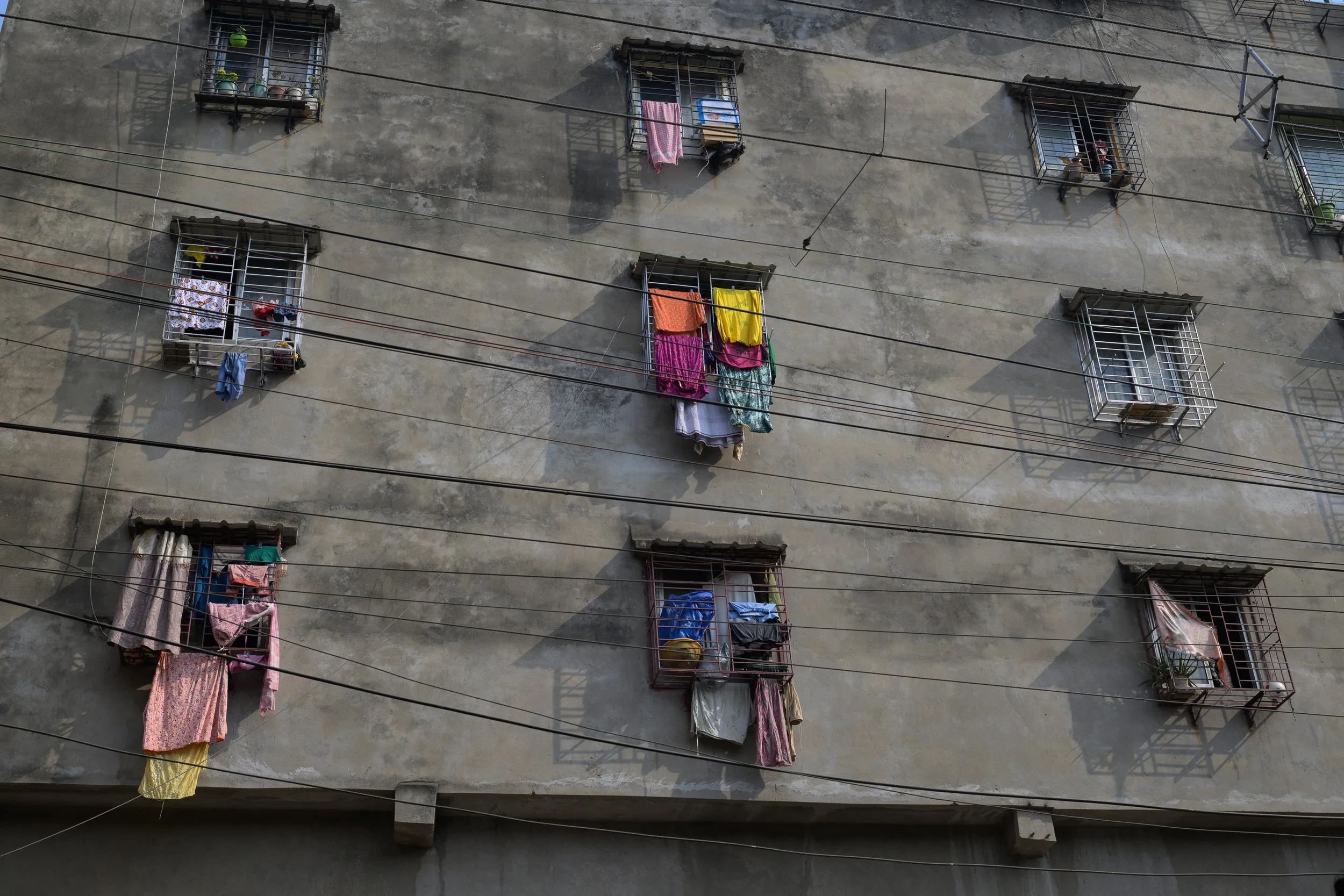 Apartment building with open windows, some with bars, and colorful laundry hanging on windows and lines outside.