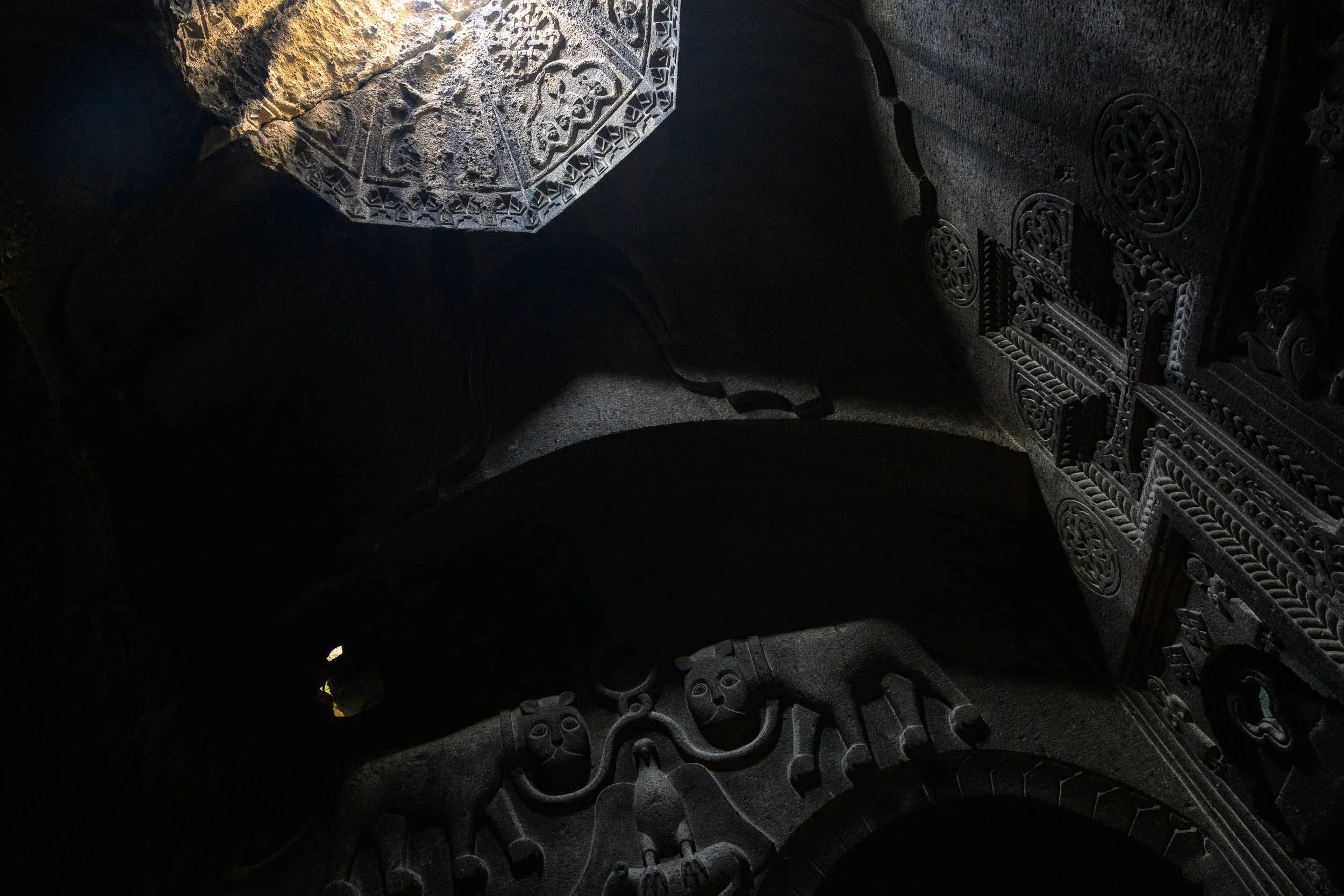 Close-up of intricately carved stone blocks and sculptures, illuminated by a beam of light, revealing detailed patterns and designs on ancient stonework.