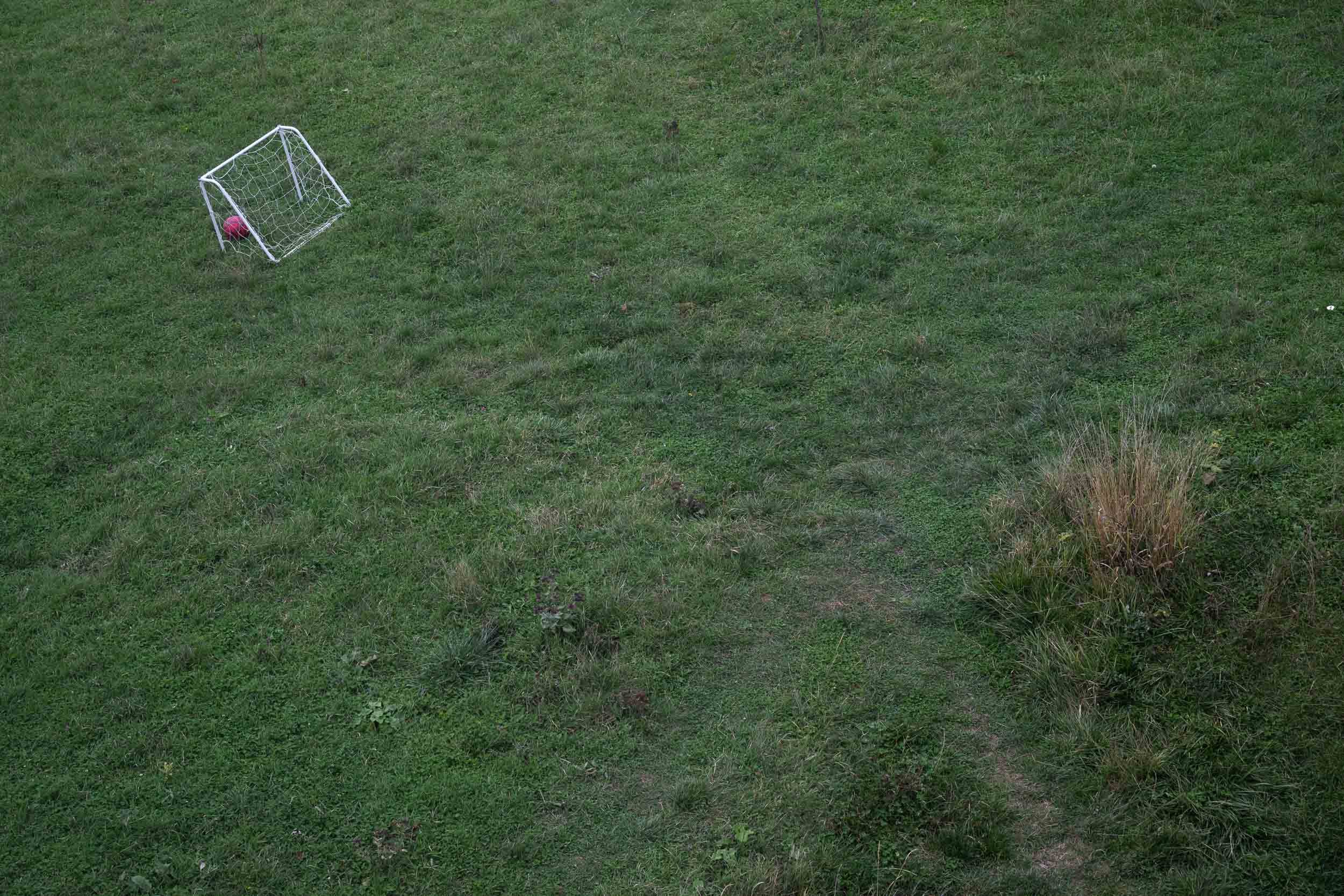 A small white soccer goal with a red soccer ball inside on green grass in an open outdoor area.