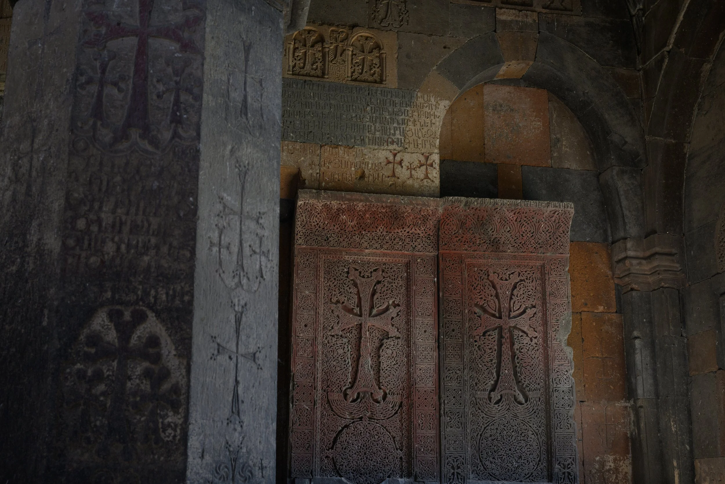 Ancient stone wall with carved crosses, script, and coats of arms in a historical church or cathedral.