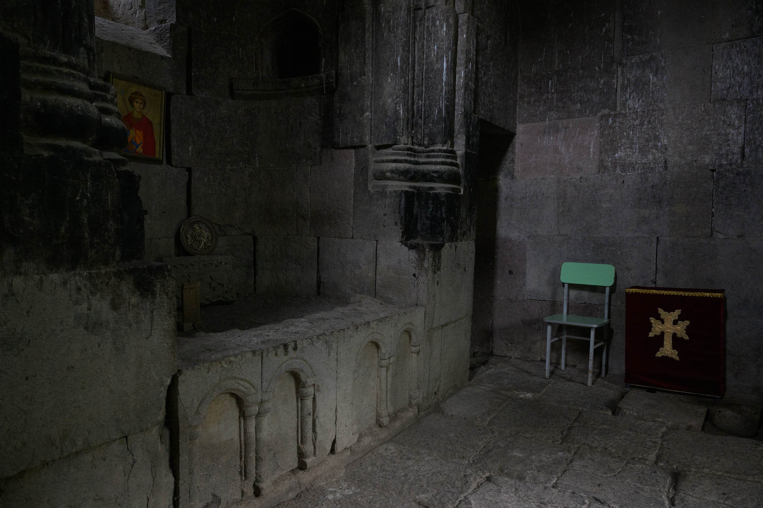 Interior of an ancient stone church or cathedral, with stone walls and altar, religious icons, and a green chair.