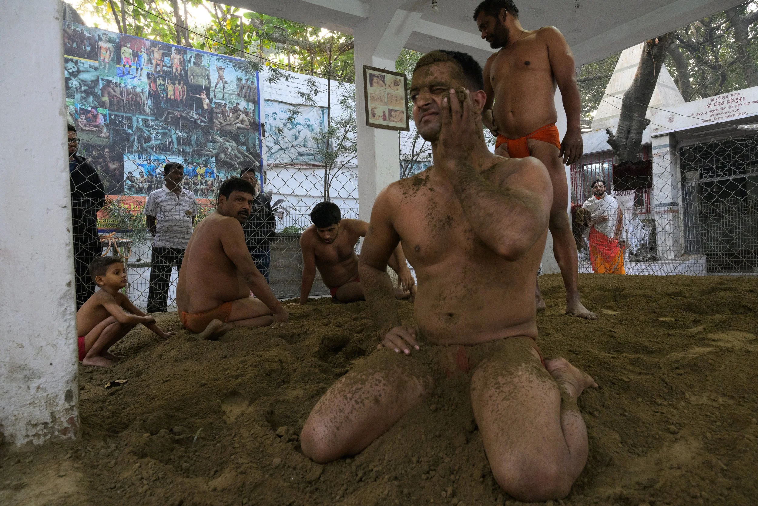 Men engaged in a traditional Hindu ritual known as 'Potath' or 'Kumkum Abhishekam', where they anoint each other's faces with turmeric paste inside a temple. Several onlookers, including children and adult men, observe the ceremony. The setting is a 