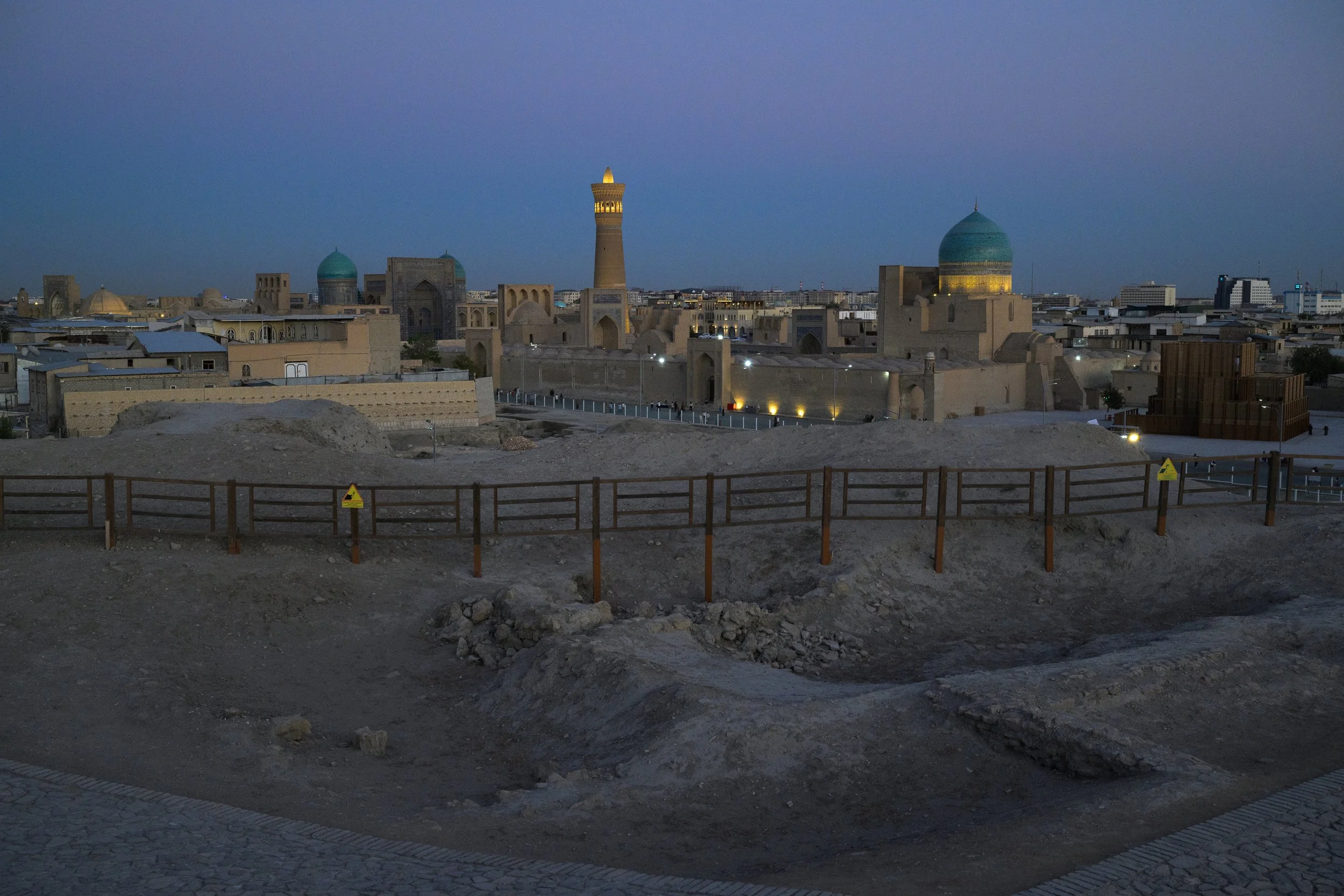 Cityscape of ancient architecture at dusk with mosques, minarets, and domes, under a sunset sky, in a Middle Eastern city.