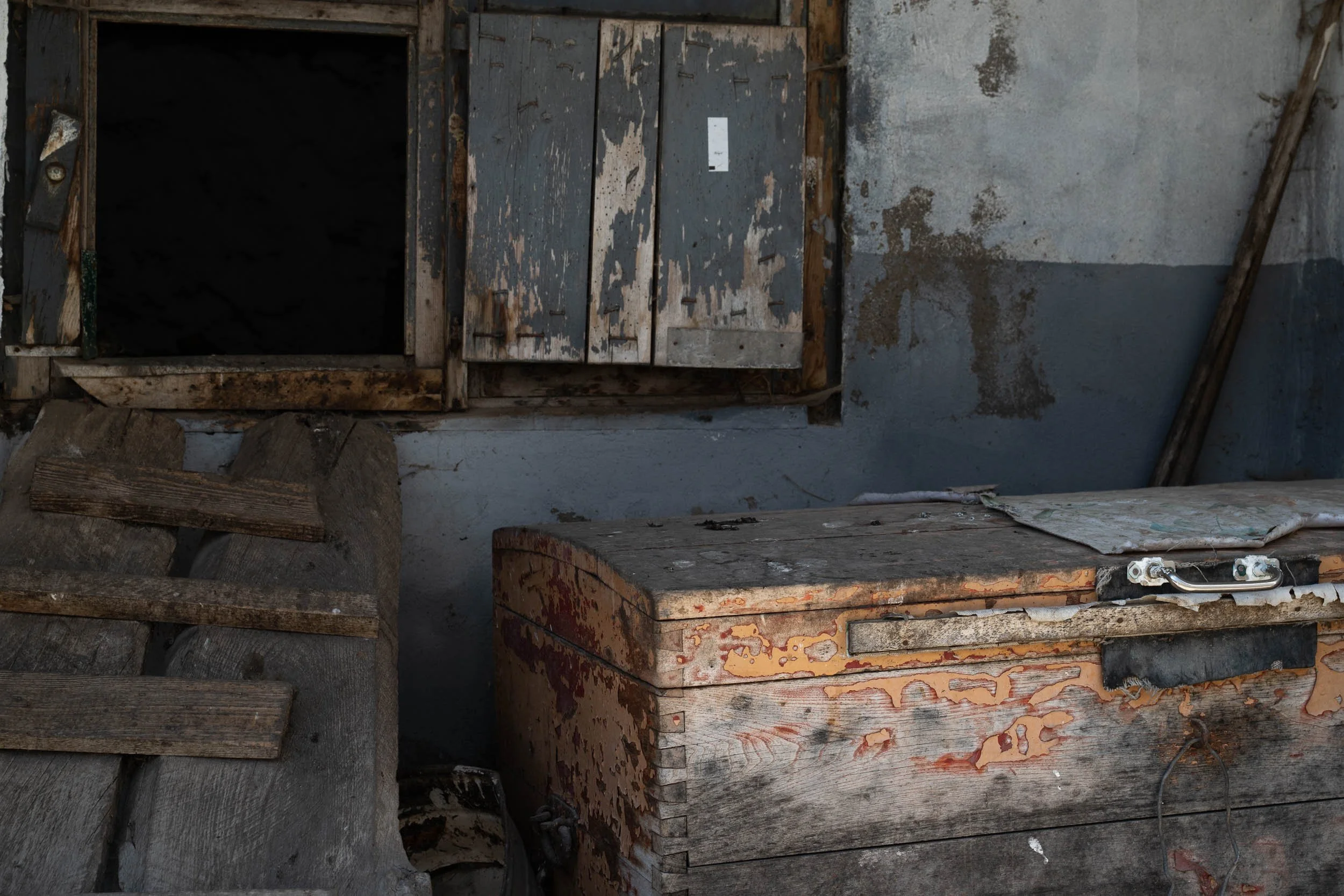 Old, weathered wooden boxes and crates with peeling paint and rust, placed against a wall in a rustic, abandoned setting.