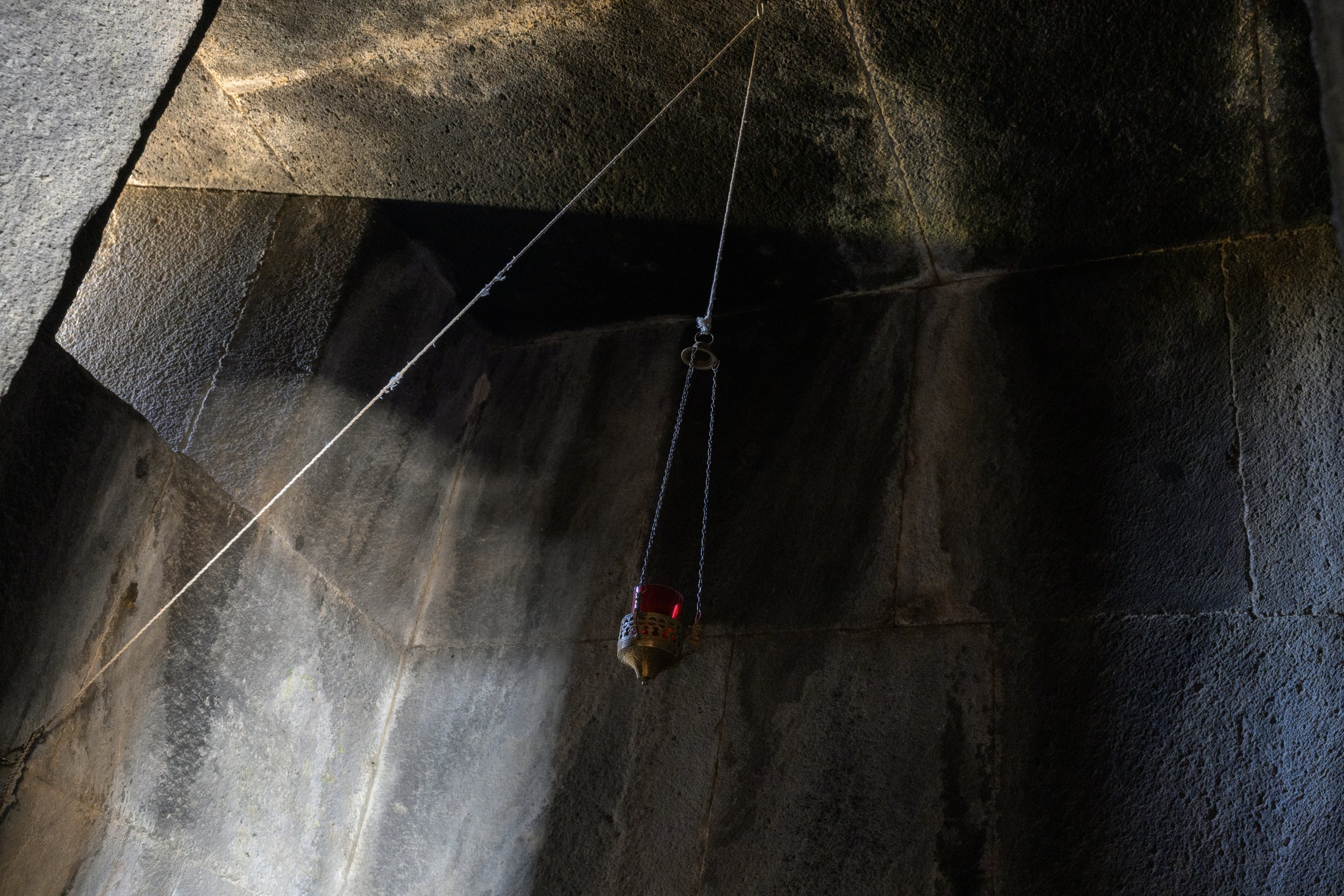Inside view of a stone structure with a hanging oil lantern suspended by chains, attached to a thin white wire.