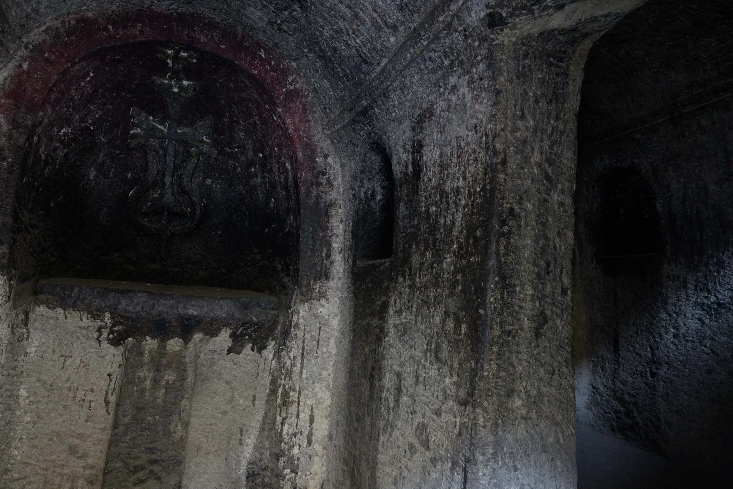 A dark, ancient stone underground tunnel with arched walls and a small opening in the distance.