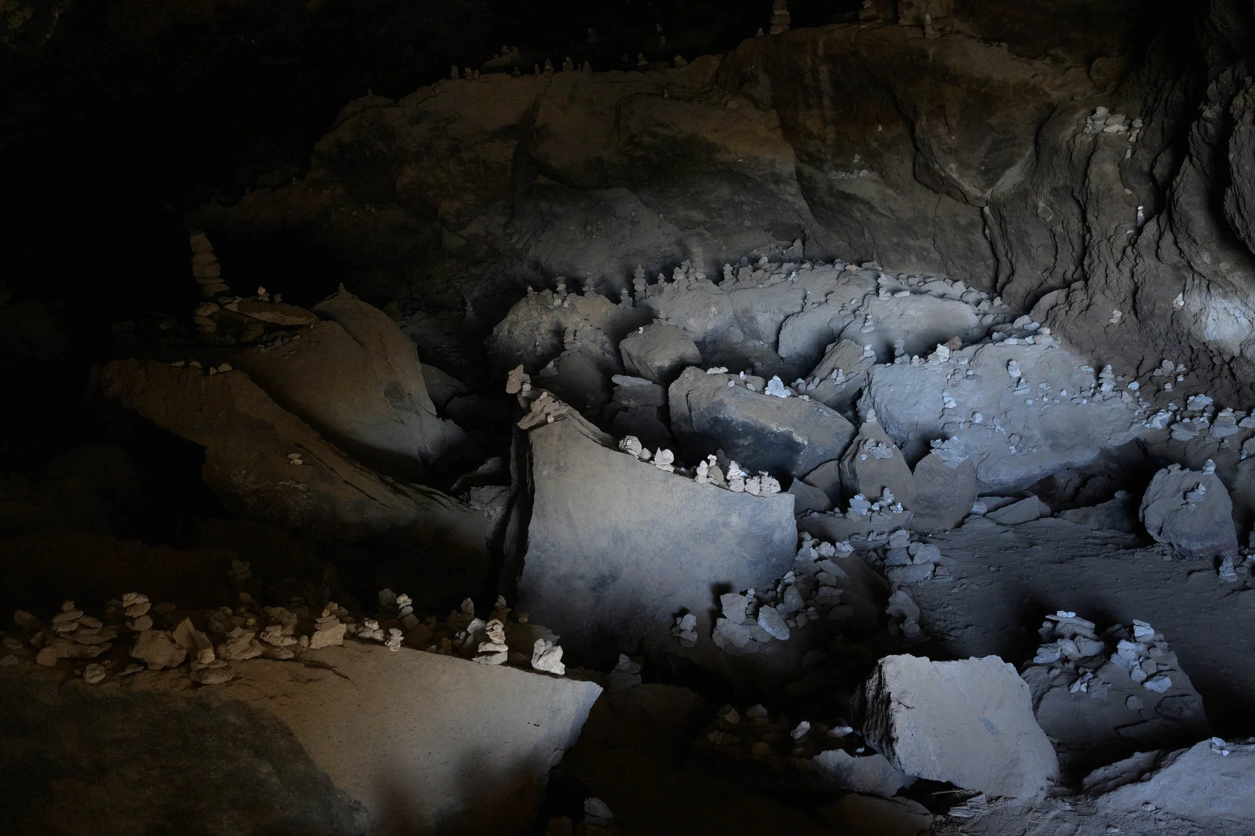Illuminated rock formations with visitor-placed stone cairns inside a dark cave interior.