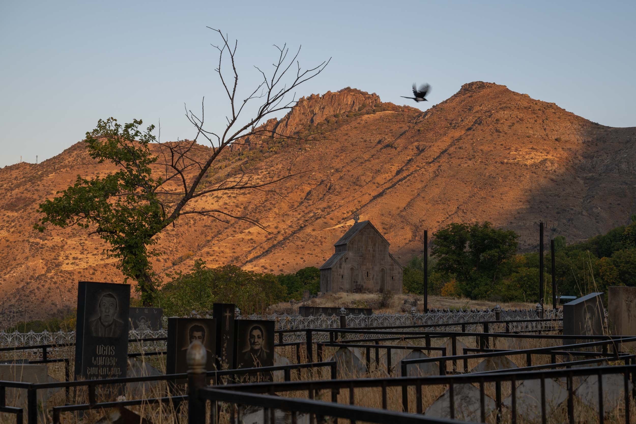 Mountain landscape with a bird flying, a church, and a cemetery in the foreground.