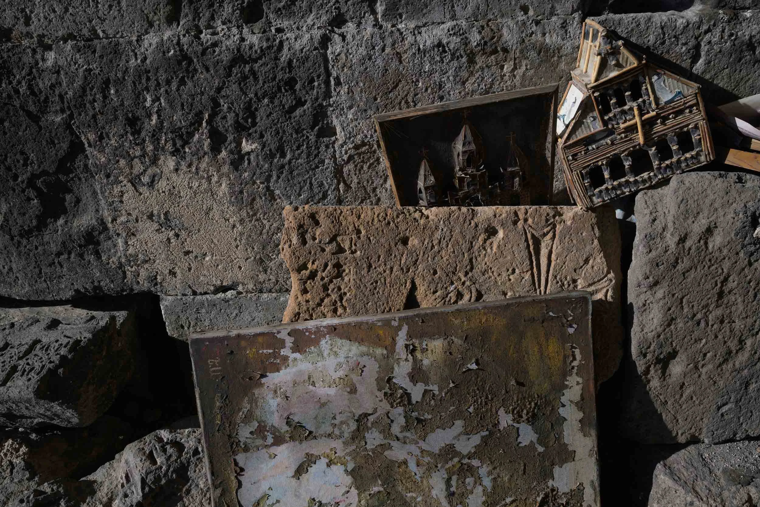 A collection of miniature model ships and a small shipwreck in a dug-out area with dark, textured soil.