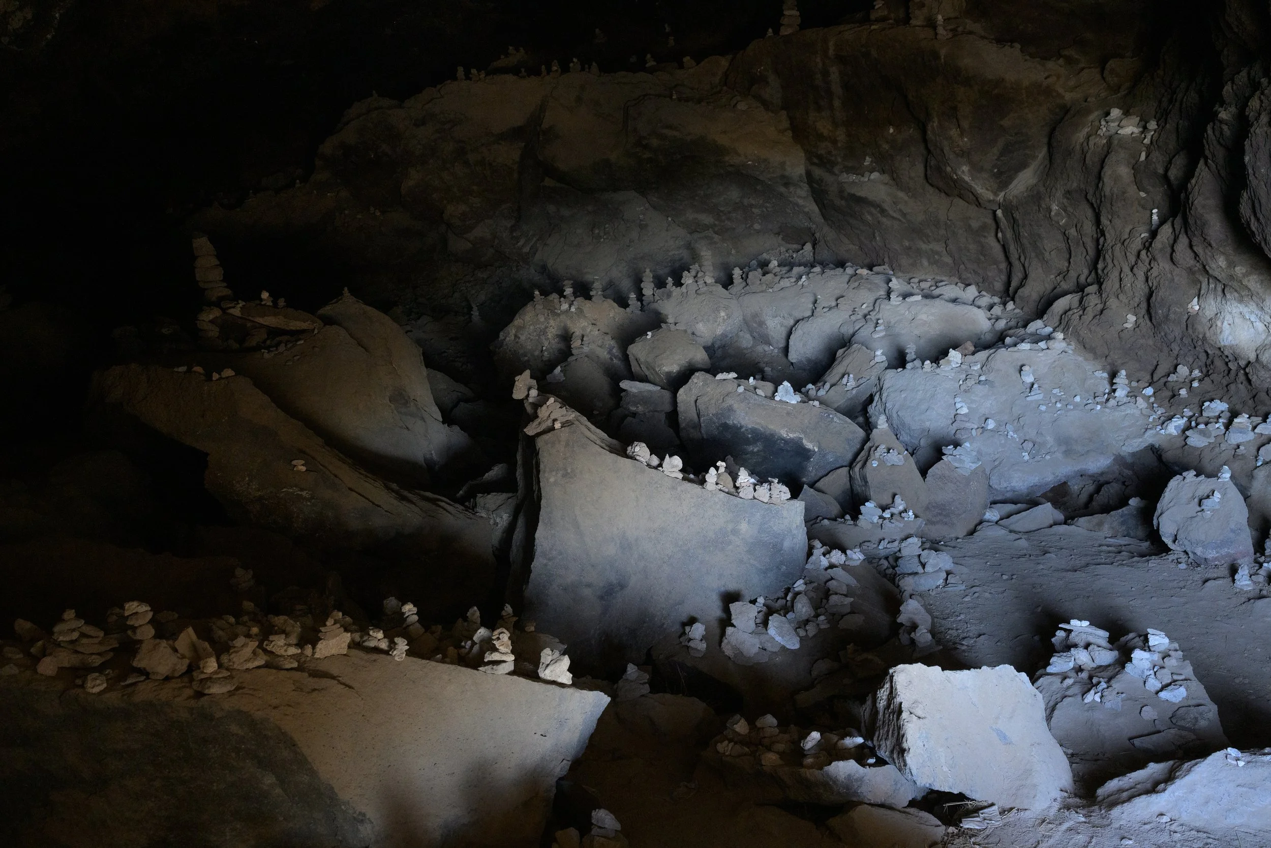 Dark cave interior with large rocks and small white mineral deposits.