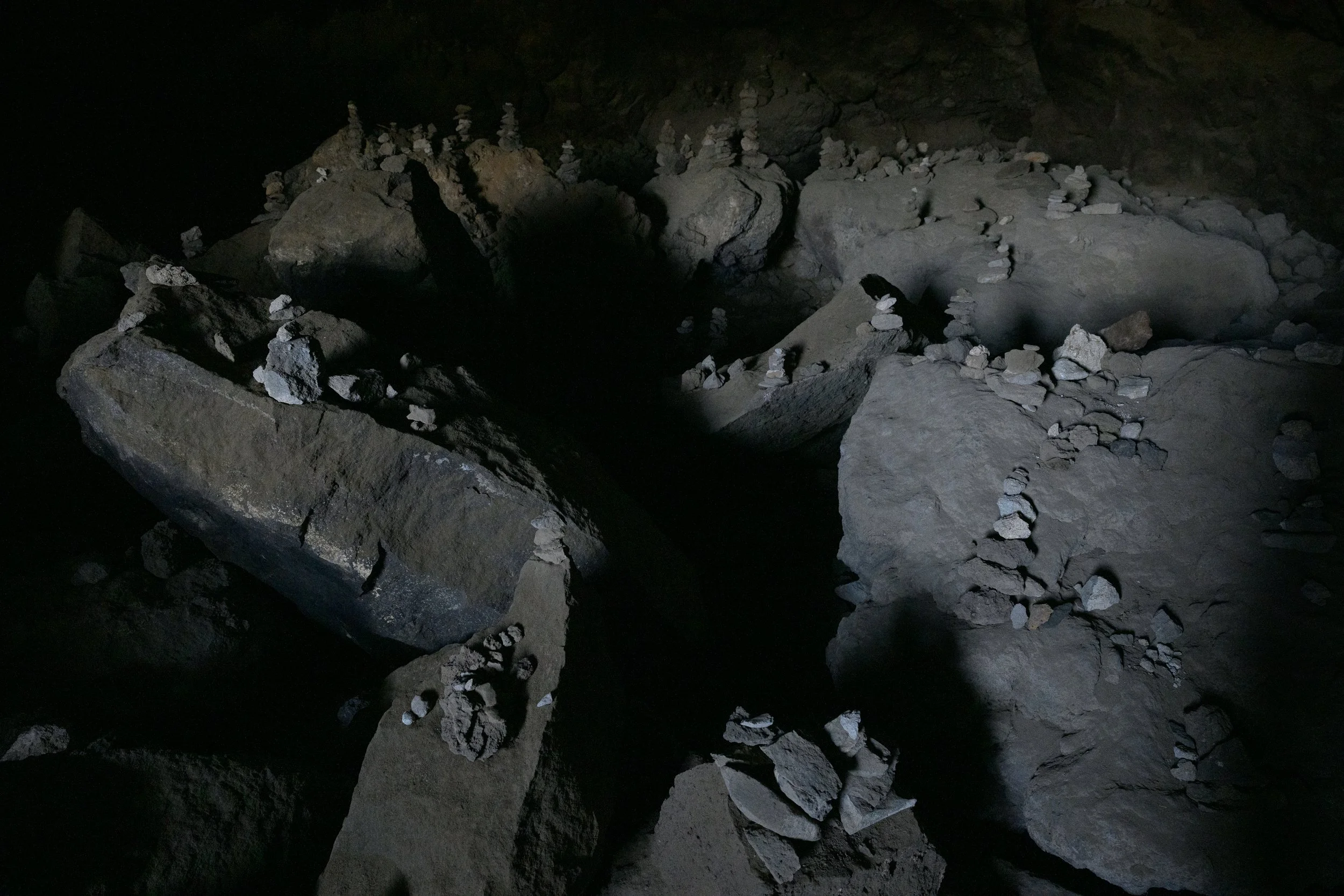 Dark cave with large rocks and formations, illuminated by a limited light source.