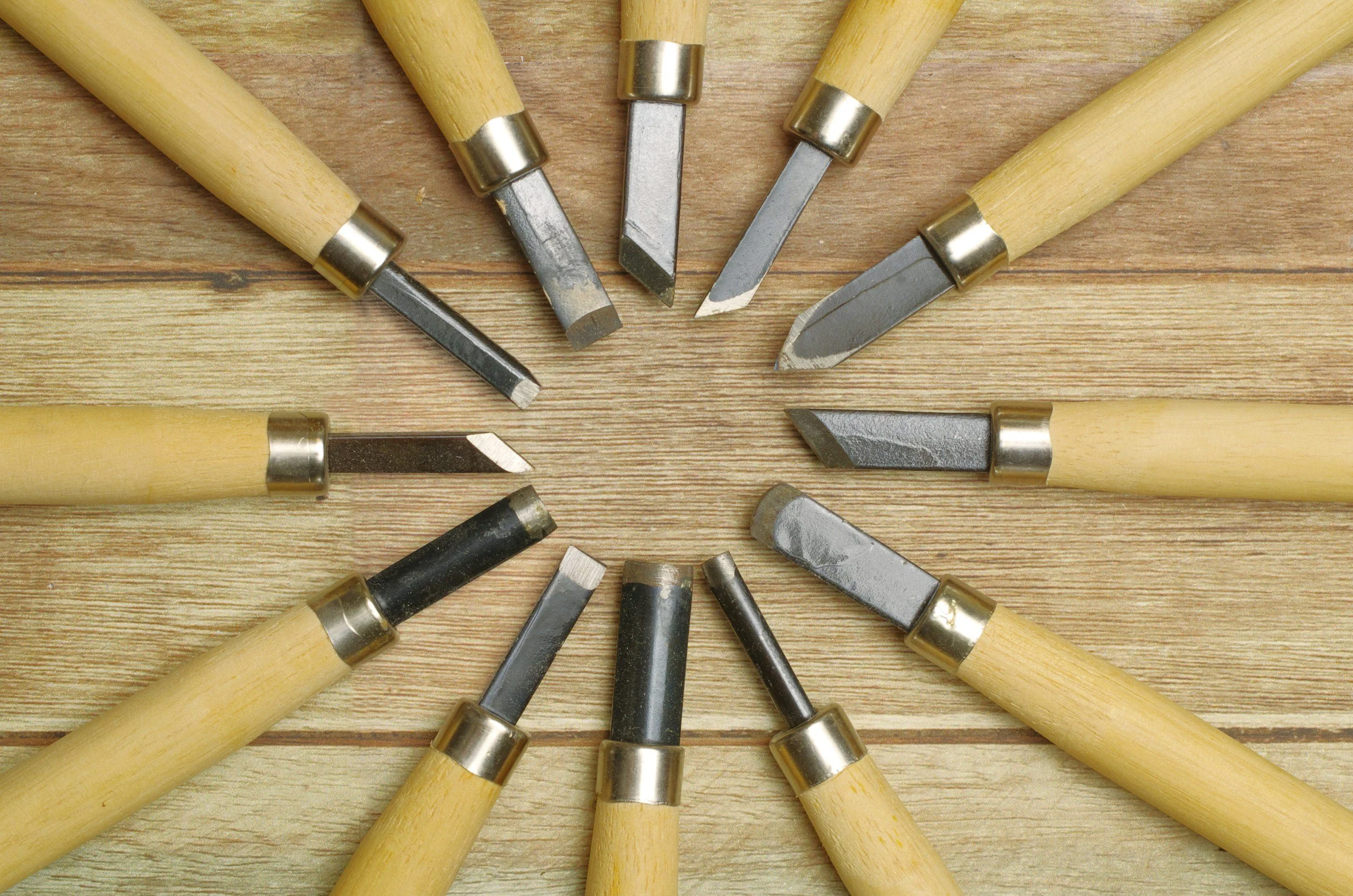 A circular arrangement of various chisel tools with wooden handles and metal blades on a wooden surface.