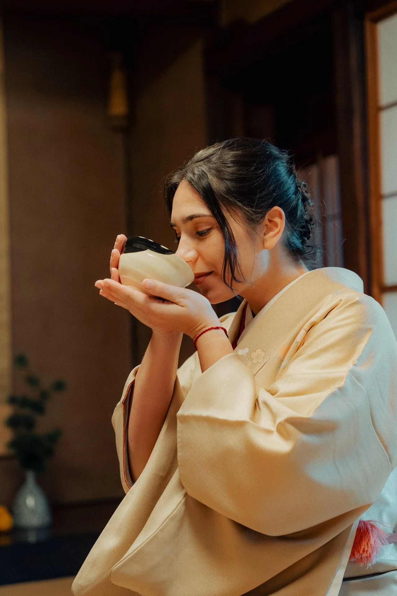 A woman in traditional Japanese kimono smelling tea from a teacup in a tea room.