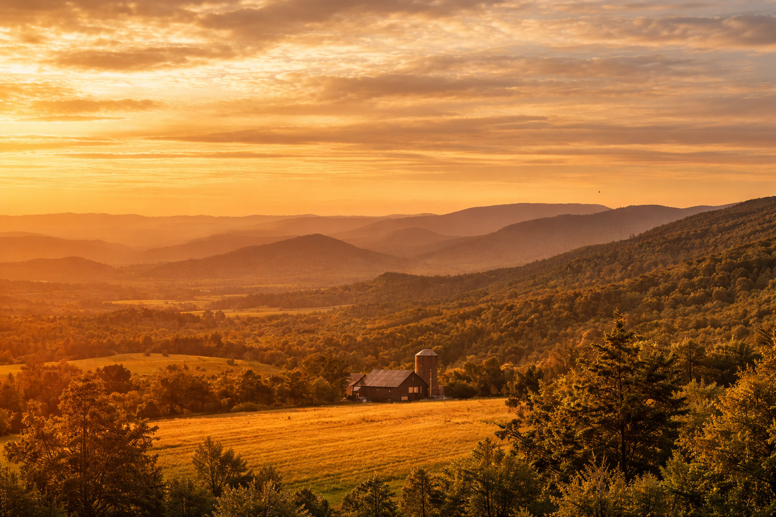 A scenic view of a farm with a barn and silo surrounded by rolling hills and trees at sunset, with a sky filled with orange and yellow clouds.