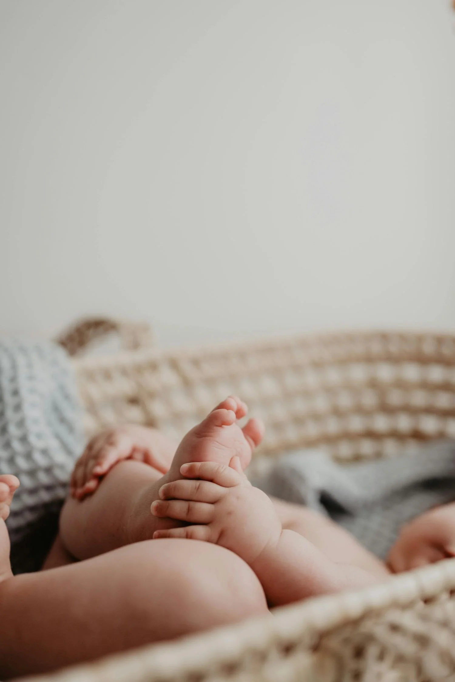Newborn baby laying in a basket, holding his feet.
