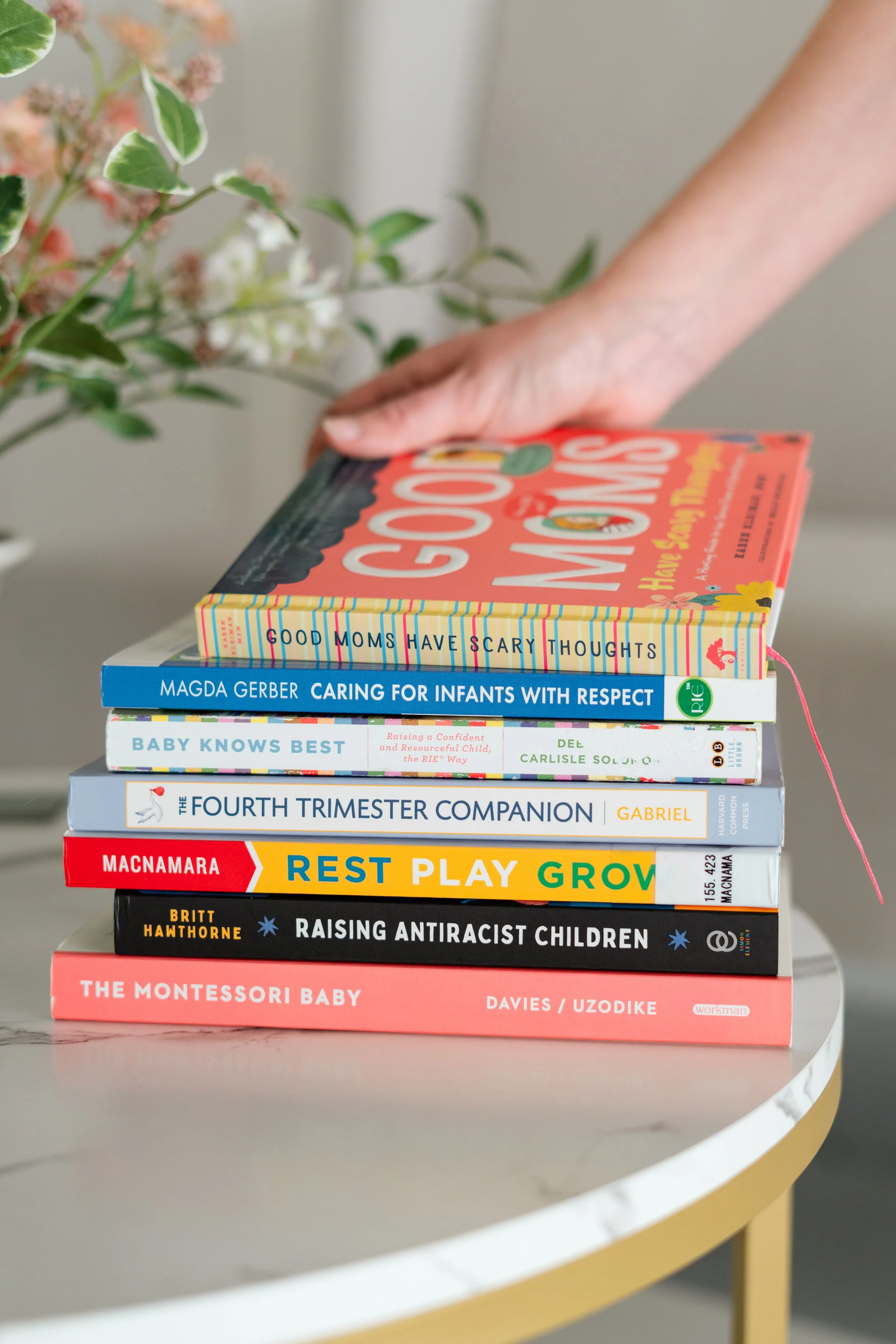 Jenna's hand placing a book on a stack of postpartum, newborn, and parenting books.