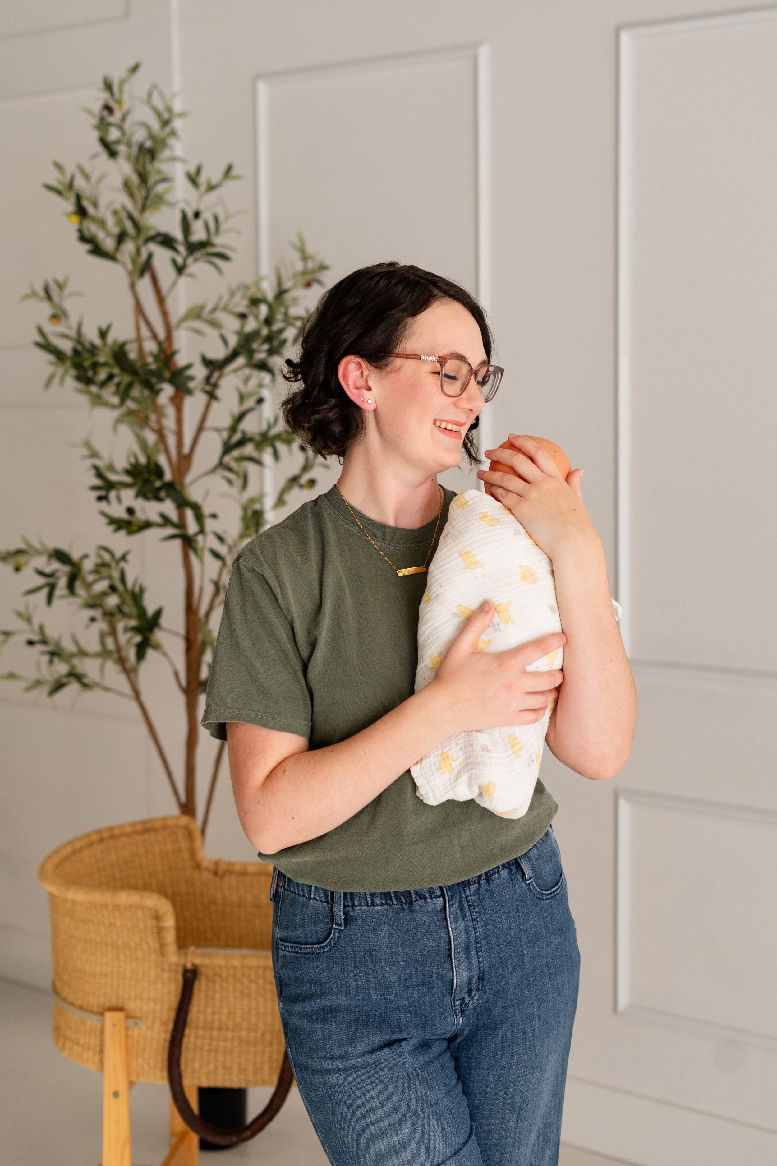 Jenna smiling while holding a swaddled newborn baby at a postpartum doula visit in Reno, NV.
