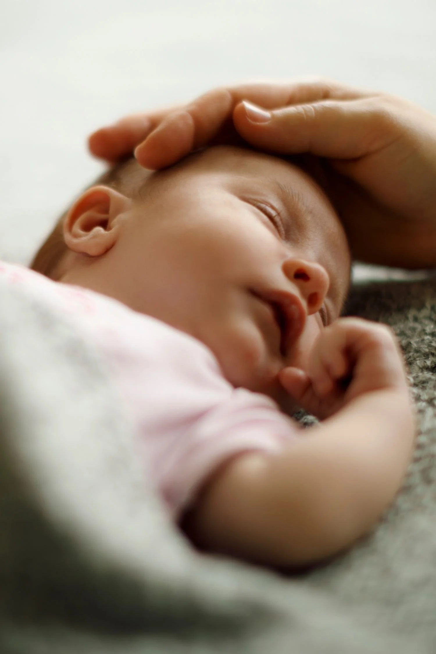 Newborn baby sleeping with mother's hand on his head.