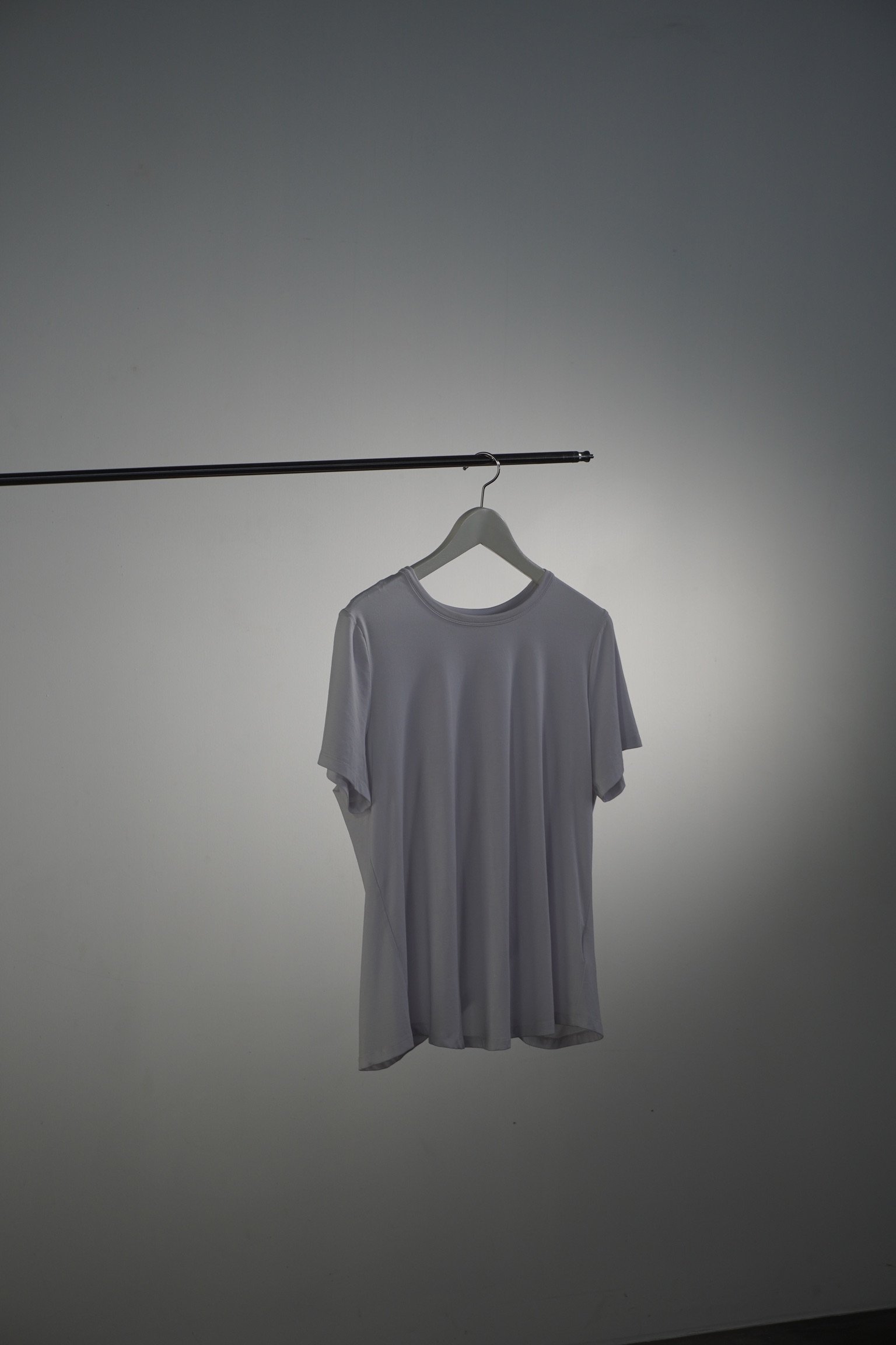 A plain white T-shirt hanging on a hanger, suspended from a metal rod against a neutral background.