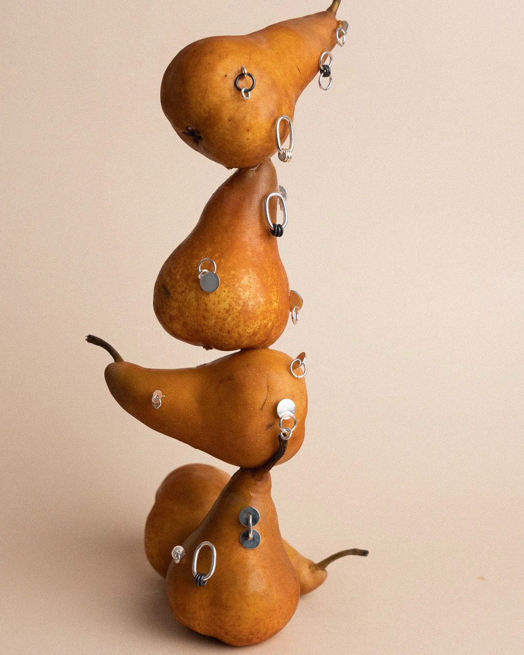 Stacked pears decorated with various metal rings and jewelry, arranged vertically against a plain background.