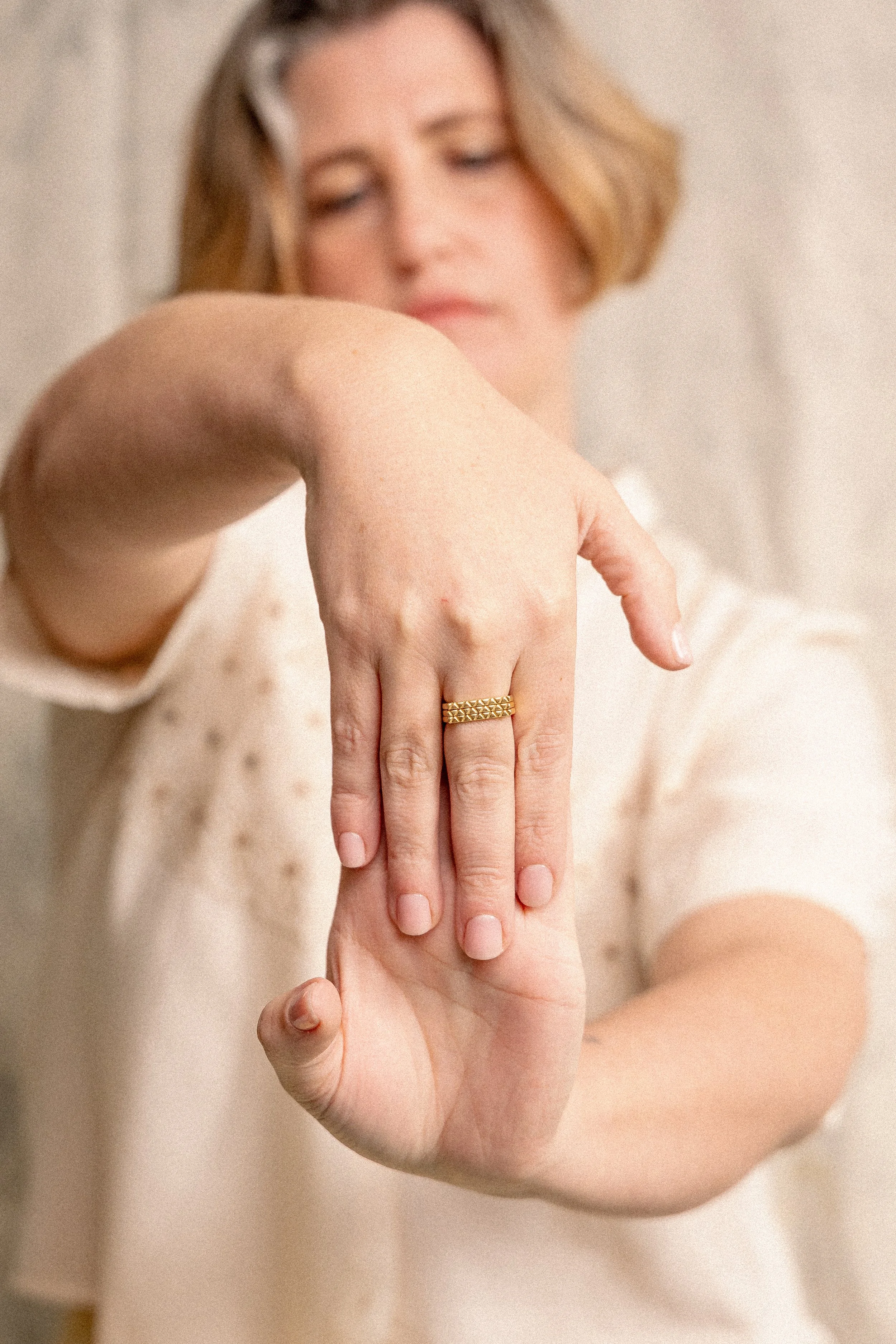 Close-up of a woman's hand with a gold ring, reaching out and touching another person's hand, in a soft, neutral-toned background.