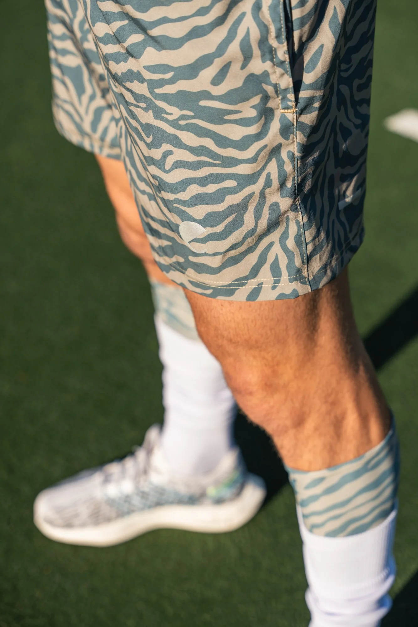 Close-up of a person wearing zebra-print shorts, standing on a grassy field, with a white shoe and sock visible, and part of a white ball on the field.