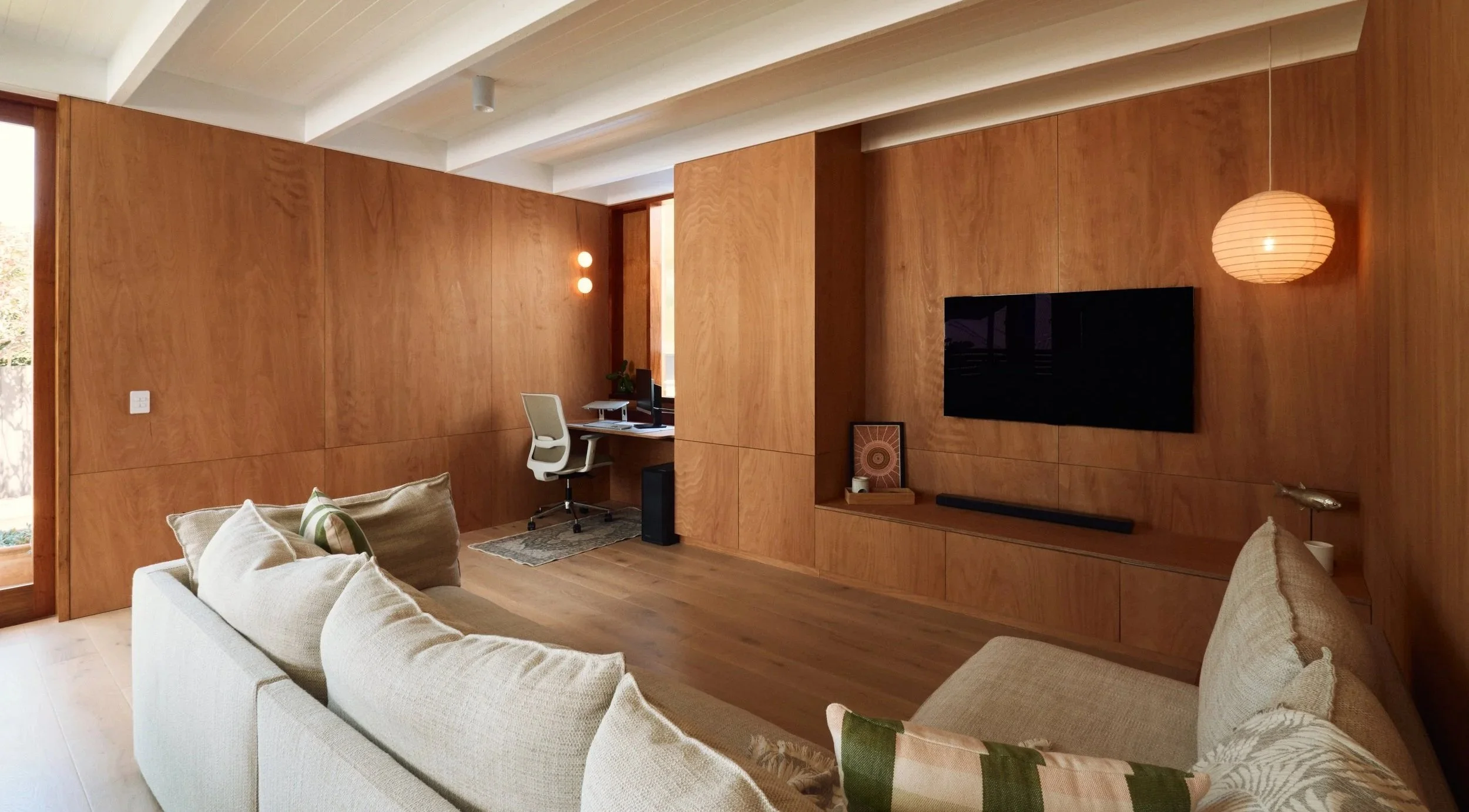 A timber walled living room with warm lighting and a TV mounted on the wall.