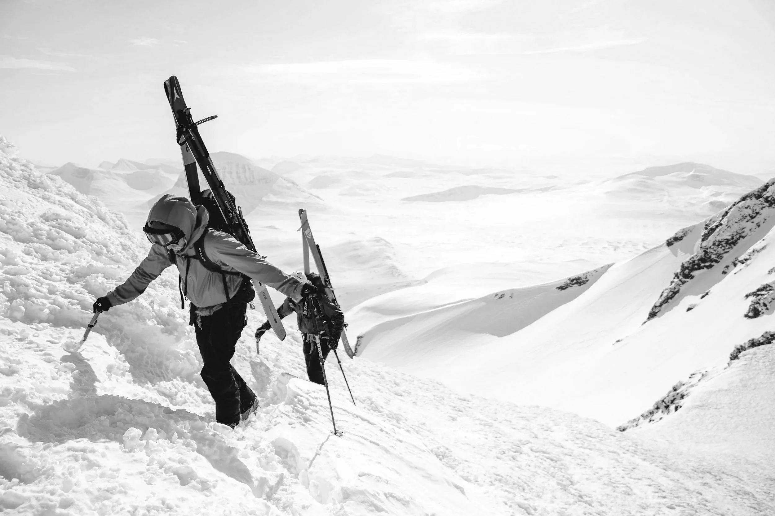 Deux skieurs en montagne enneigée, portant des équipements de ski, avec un paysage de montagnes et de neige en arrière-plan.